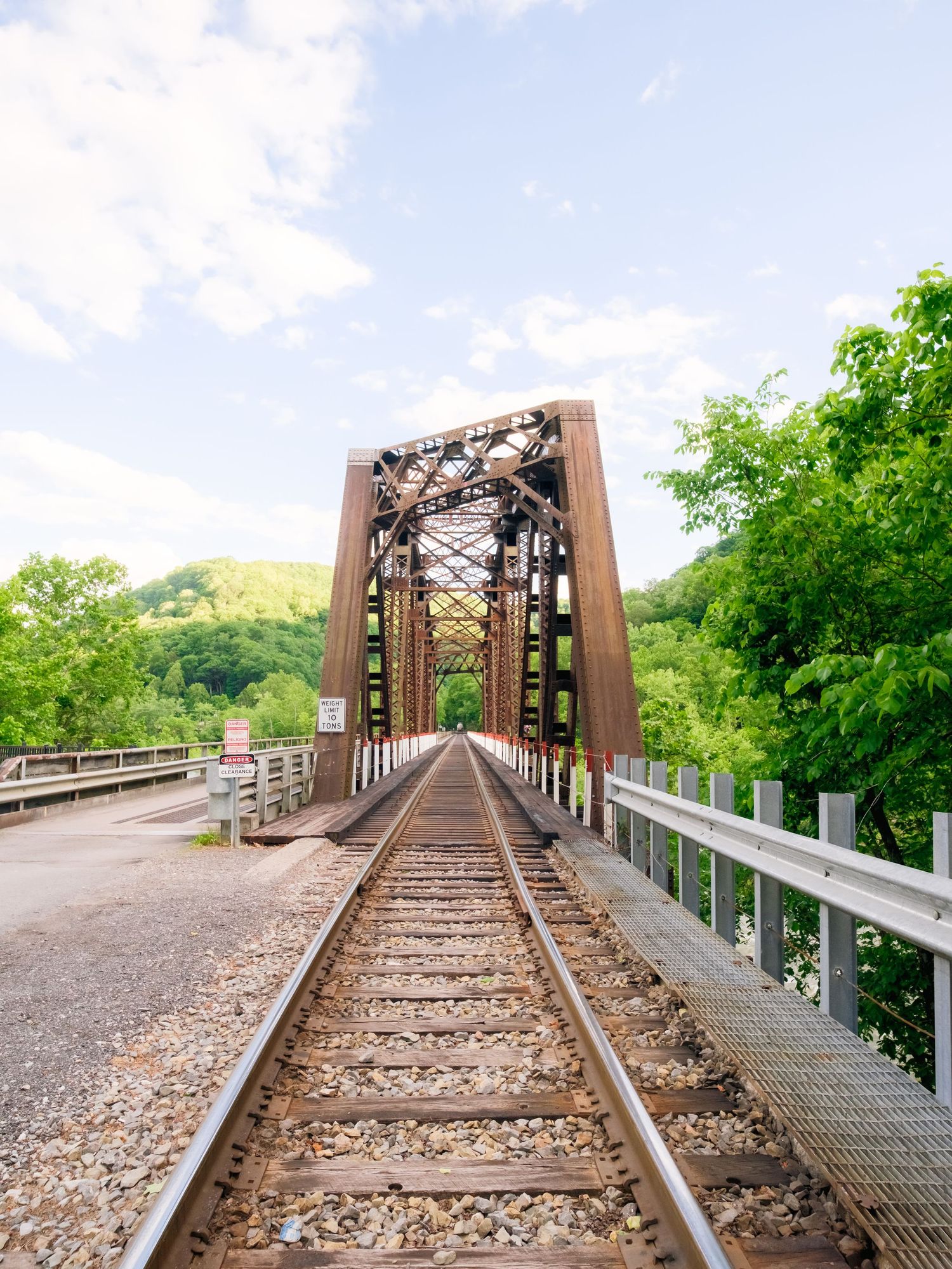 Historic railroad bridge with rusty metal trusses crosses over green landscape during spring.