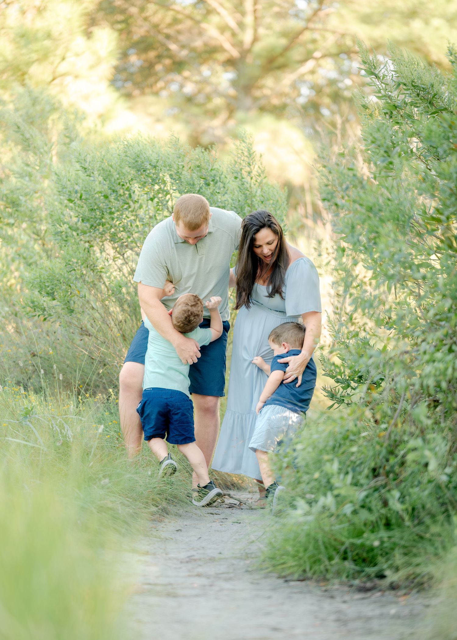 A family plays together on a sunny nature trail surrounded by lush green foliage.