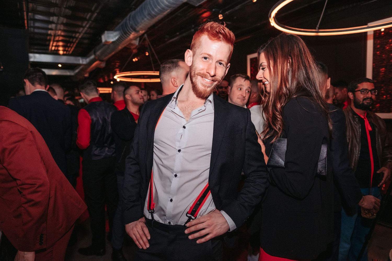 People dancing and socializing in a dimly lit nightclub with circular lighting fixtures overhead.