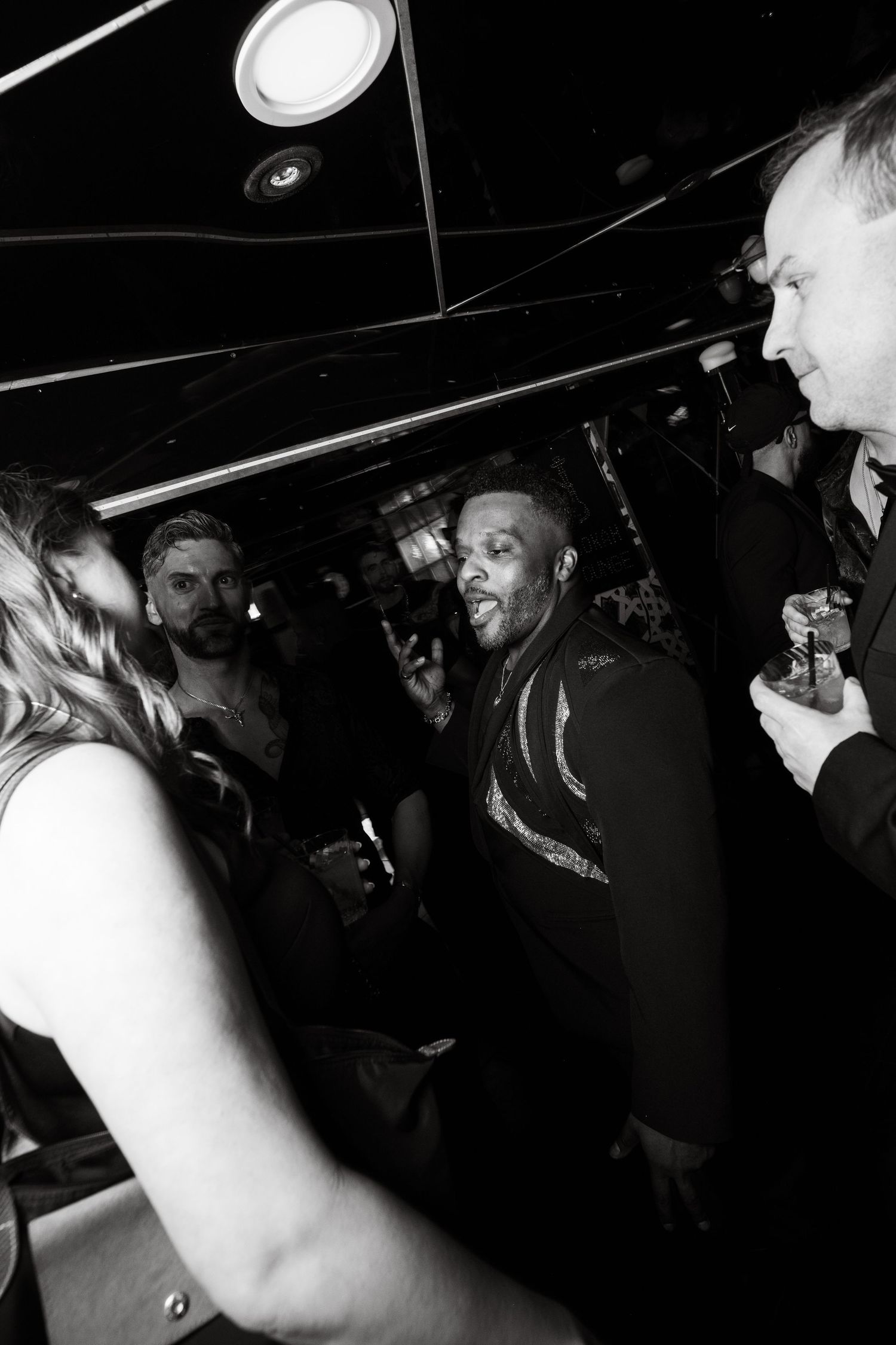 Black and white photo showing people enjoying themselves at a crowded nightclub with overhead lighting.
