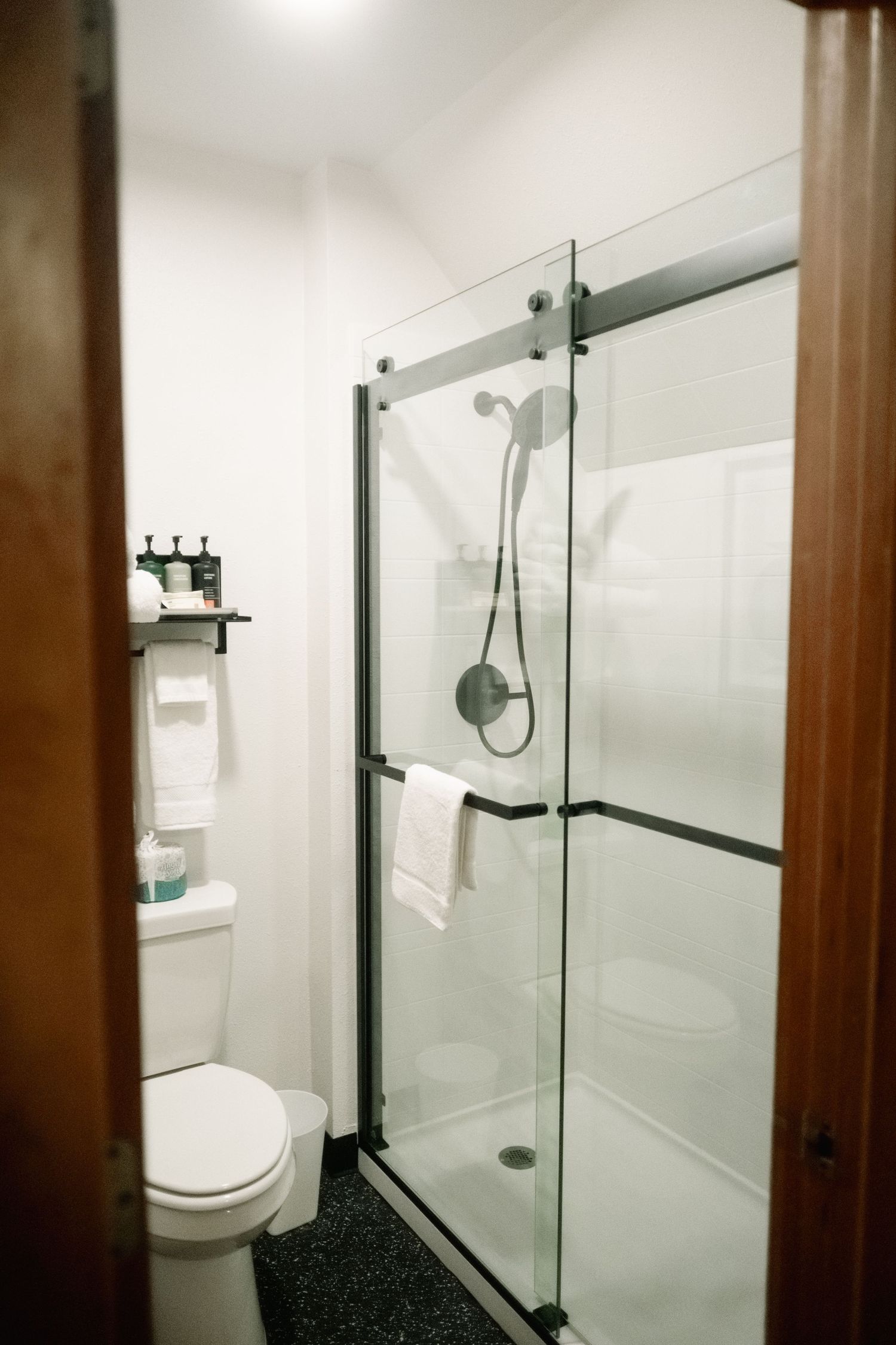 Modern white bathroom with glass shower enclosure and dark wood trim details shows clean contemporary design.