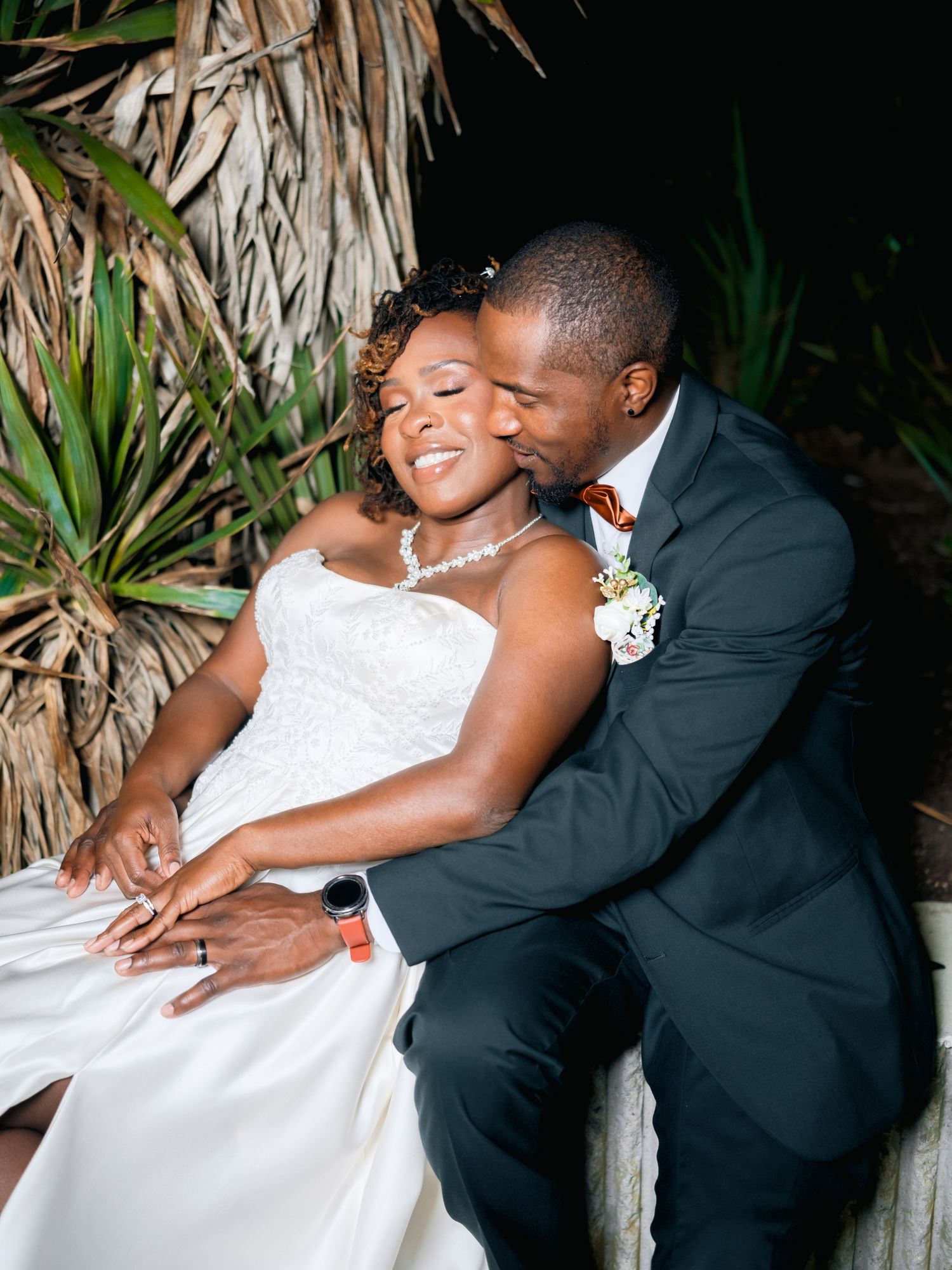 Romantic wedding portraits against tropical palm fronds showing tender embraces.
