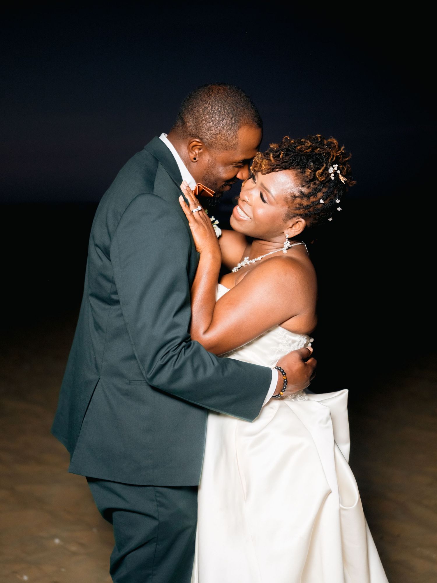 A romantic moment between newlyweds in formal attire during an evening beach wedding.