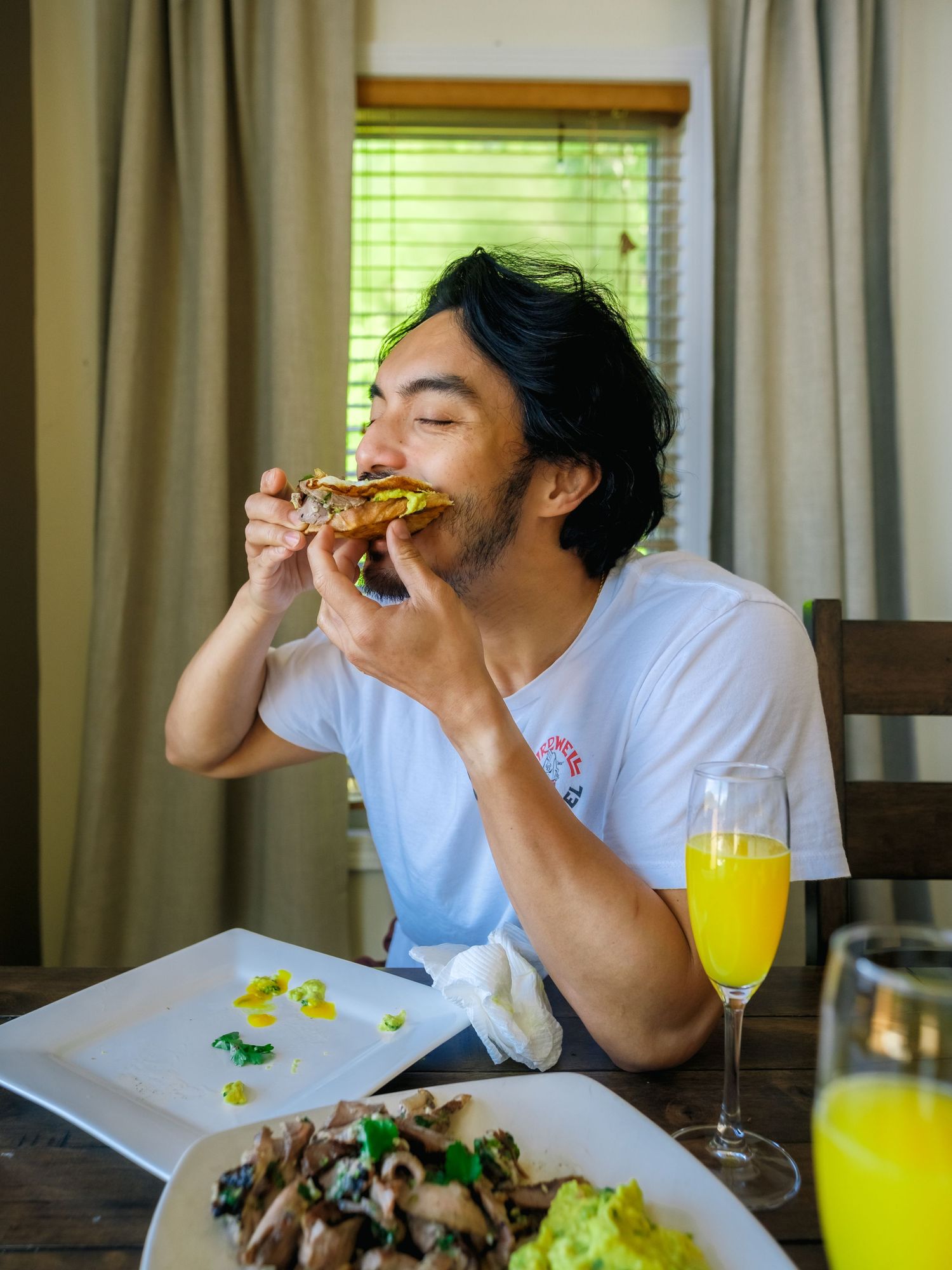 Someone enjoys a sandwich while dining with orange juice and a side salad at a sunny window table.