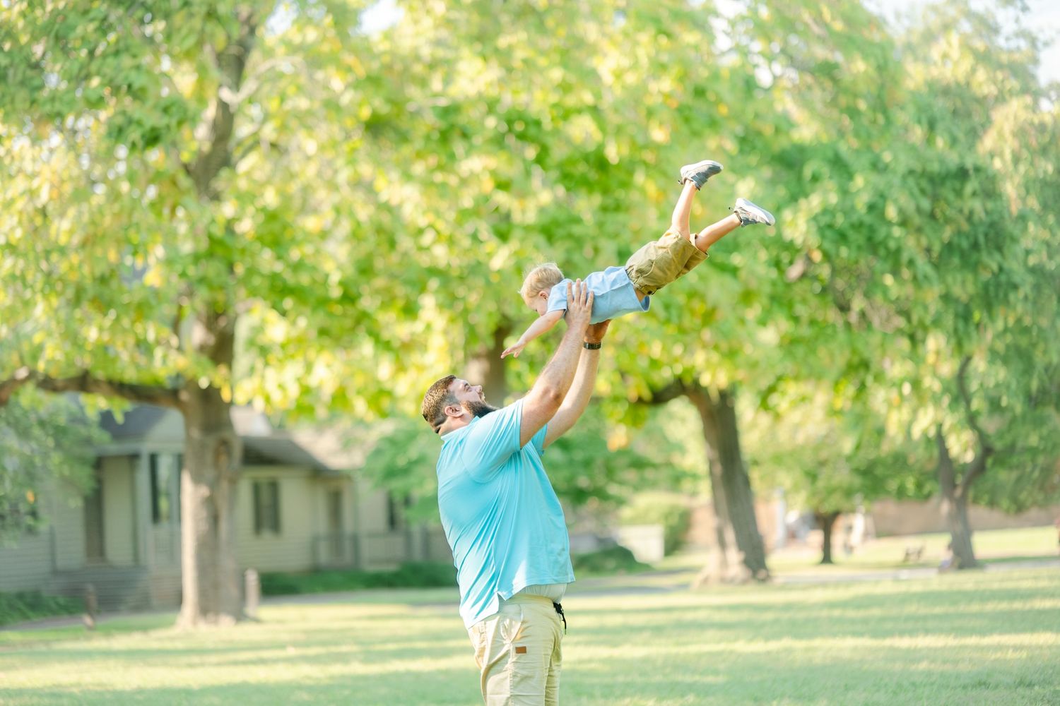 Parent tossing child high in air against sunny summer backdrop.