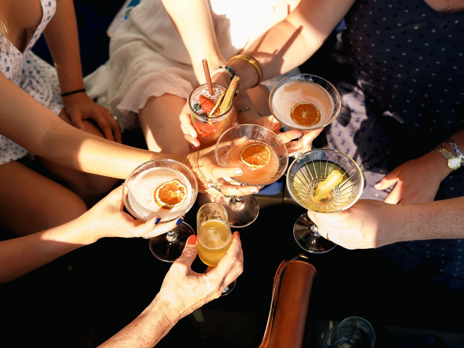 Multiple hands clinking and toasting with champagne glasses in a dimly lit setting while holding candles.