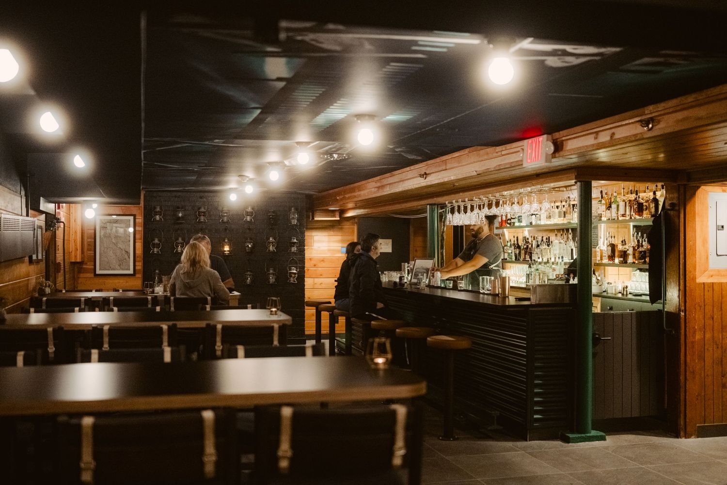 Modern bar interior with warm lighting features exposed wood beams, hanging pendant lights, and cozy booth seating.
