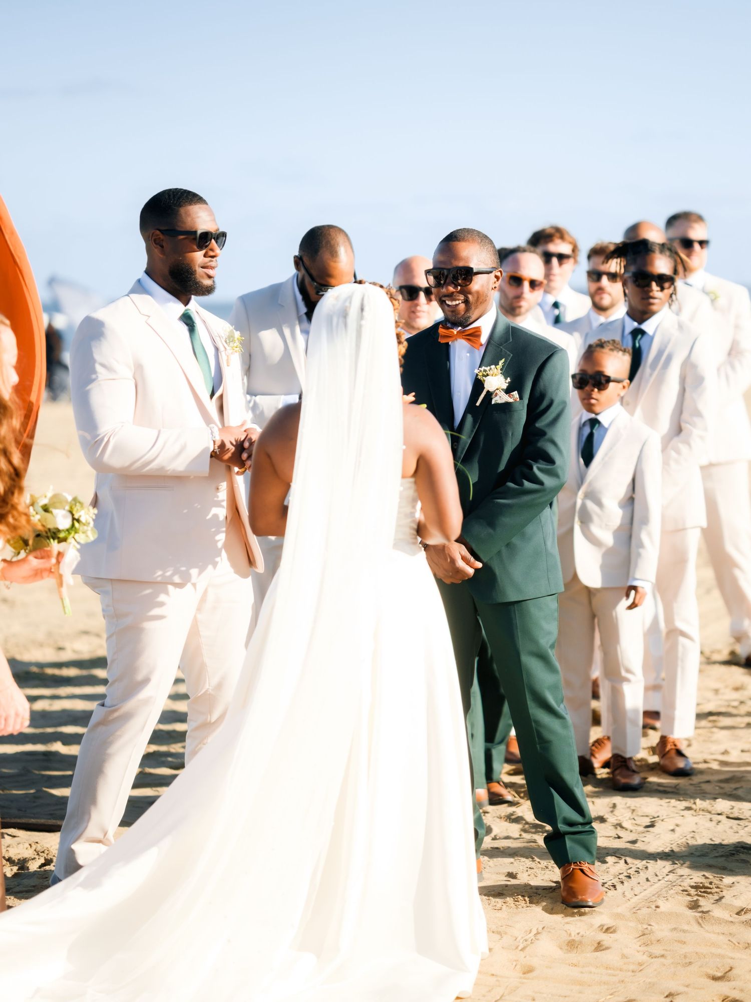 Beach wedding ceremony with guests in white attire against sandy backdrop.
