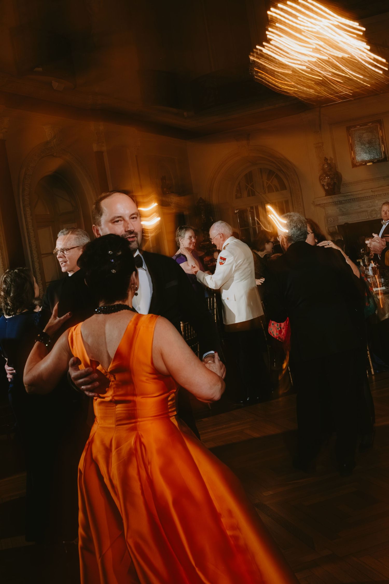A group of people dancing at an elegant evening event with warm lighting and formal attire.