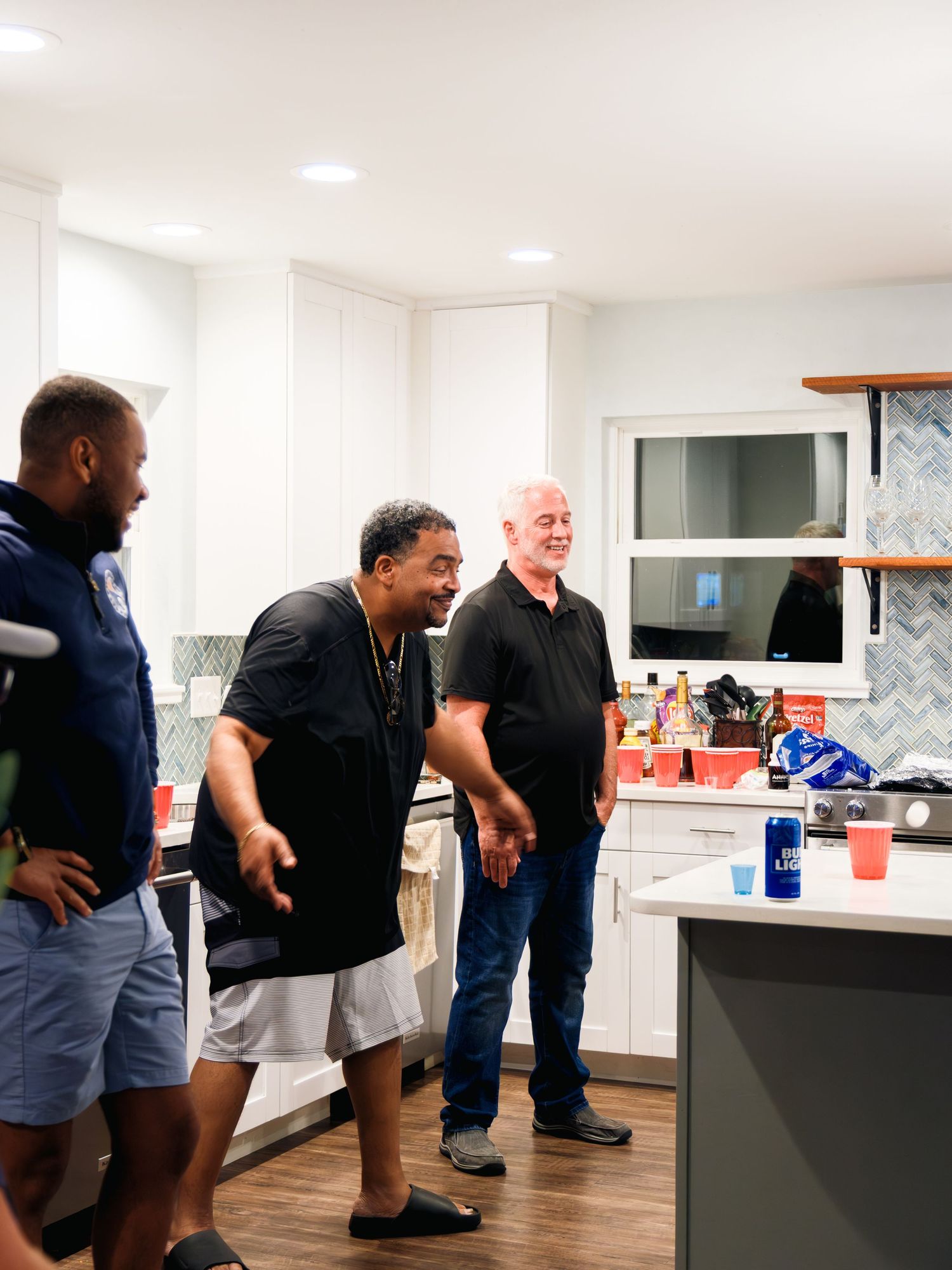 A group of people stand in conversation near a bright white kitchen island with a black countertop.