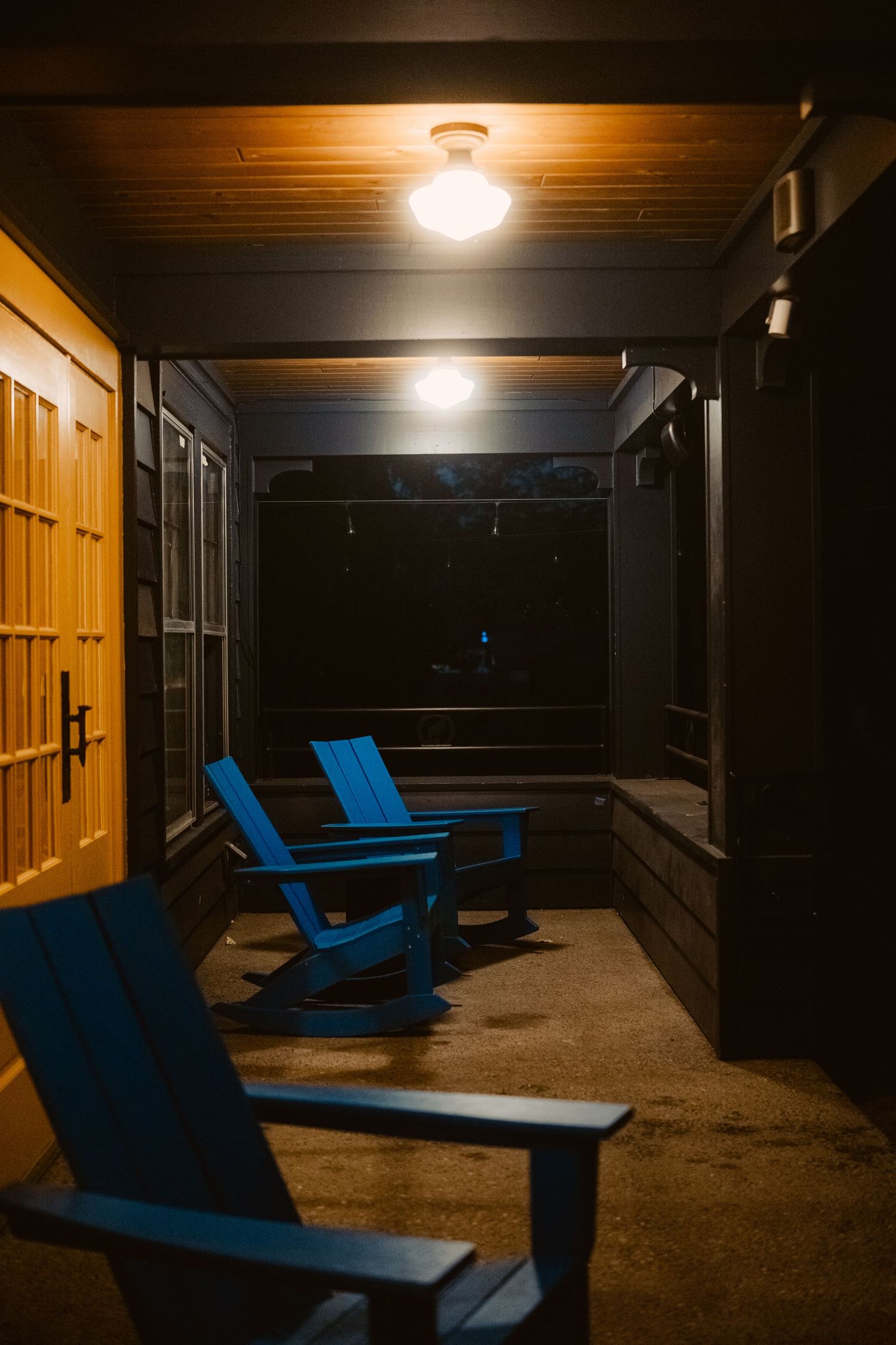 Nighttime view of outdoor patio space with bright blue Adirondack chairs illuminated by warm ceiling lights.
