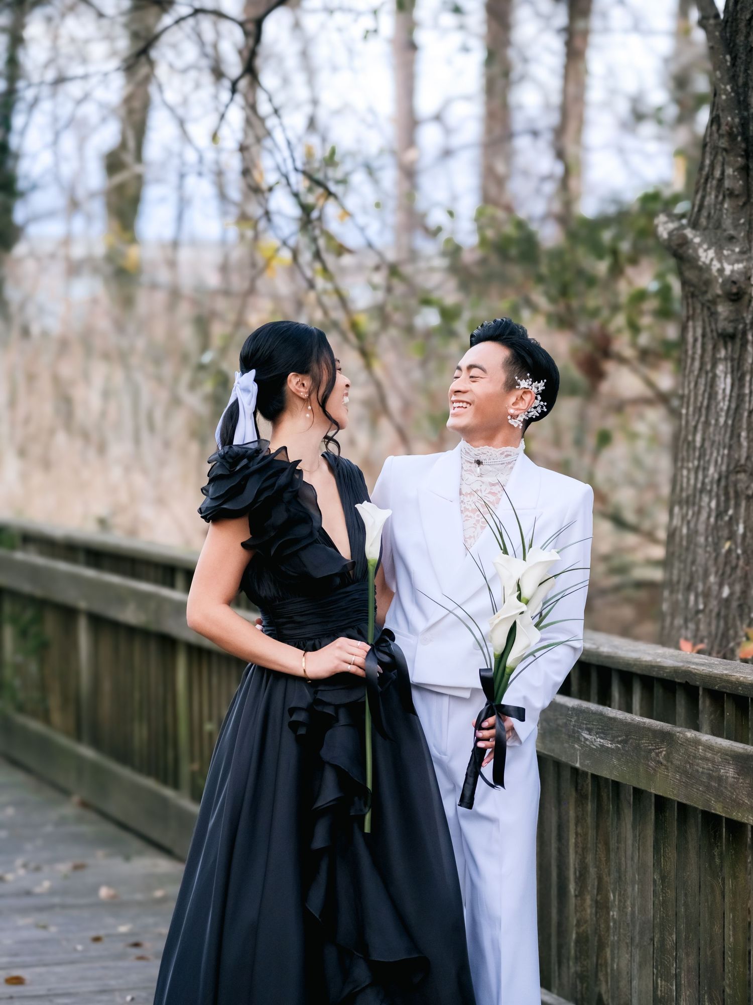 A couple in contrasting black and white outfits performs dramatic dance poses on a wooden walkway in nature.