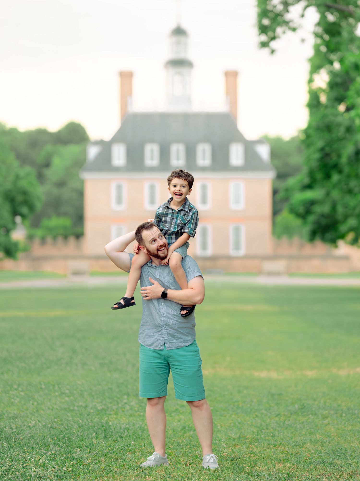 A child sitting on shoulders in front of the historic Governor's Palace building at Colonial Williamsburg on a sunny day.