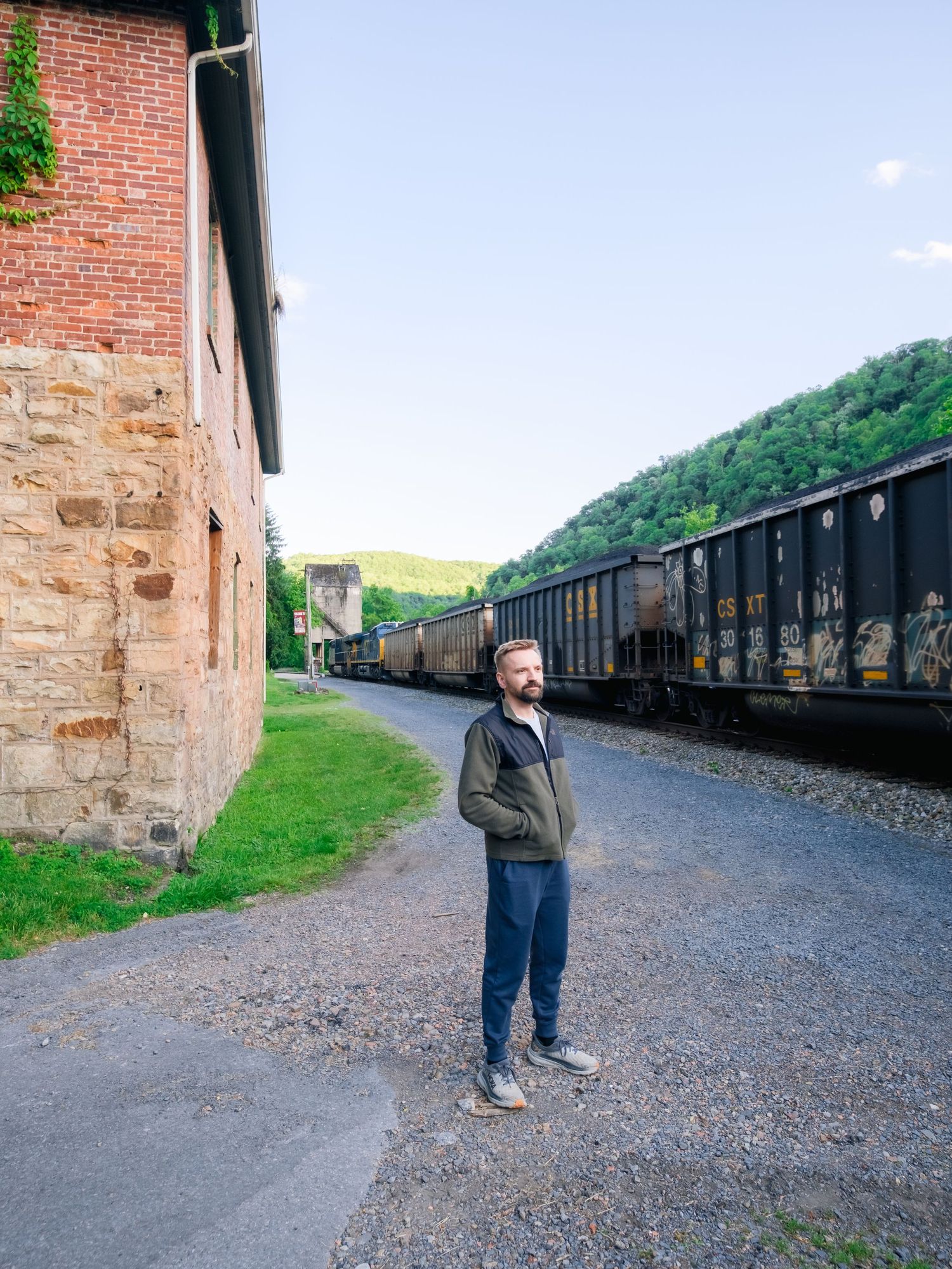 A series of four images showing someone walking along an abandoned railway line with vintage freight cars and brick buildings.