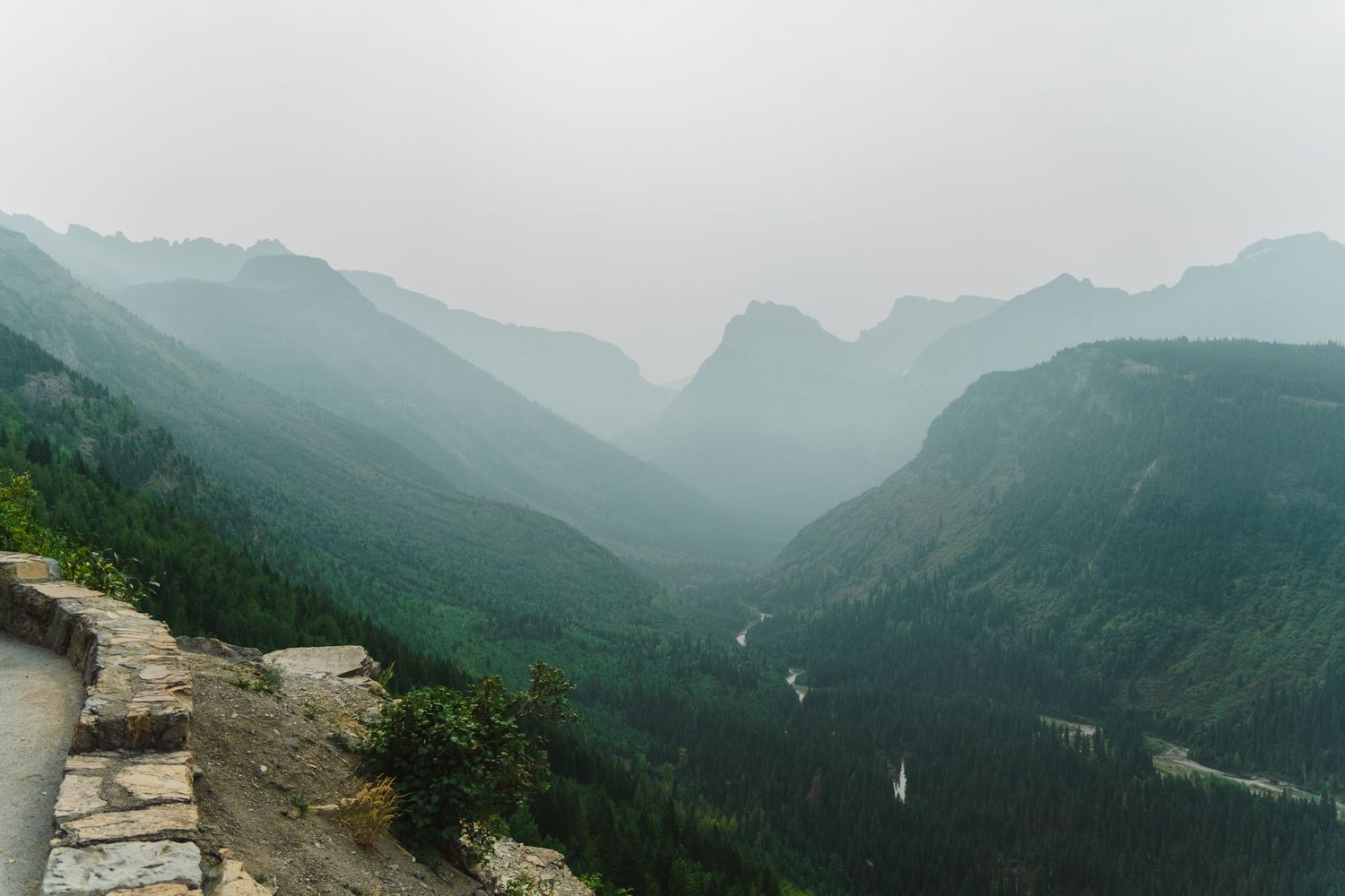 Misty mountain vista with winding guardrail overlooking a deep forested valley in Glacier National Park.