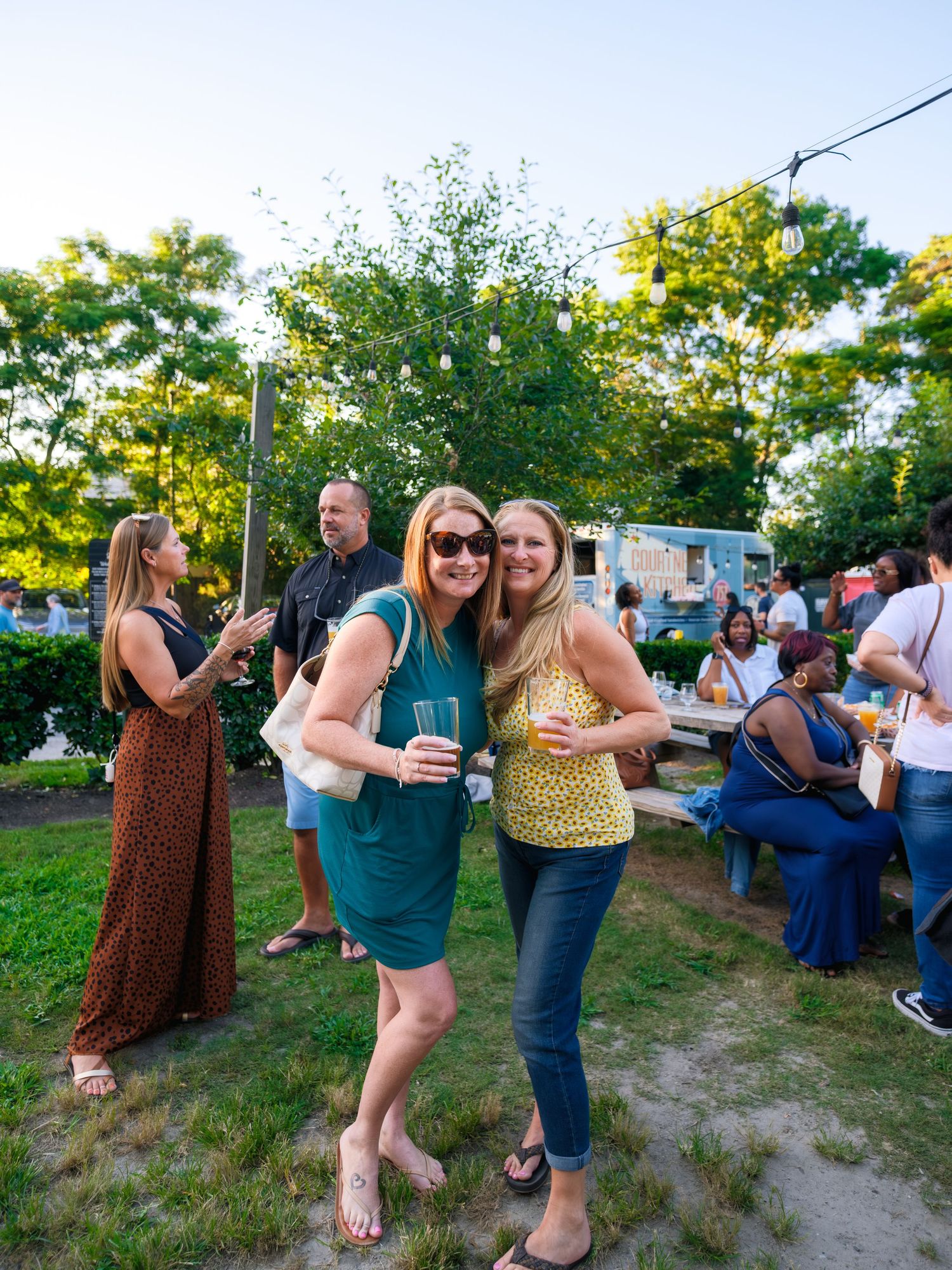 A lively outdoor social gathering with guests dancing and mingling on grassy terrain at dusk.