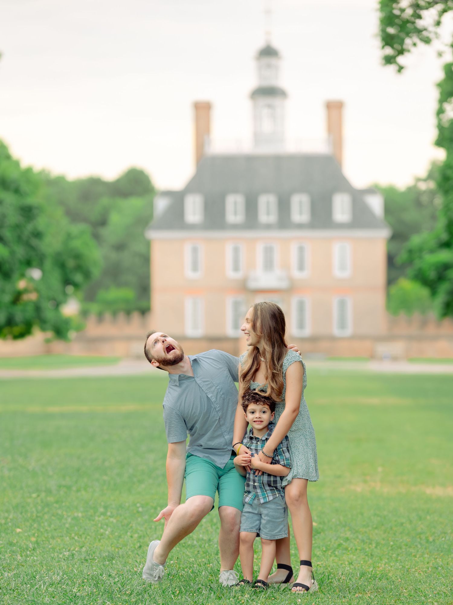 A couple shares playful candid moments on a grassy lawn with historic Colonial Williamsburg buildings in the background.