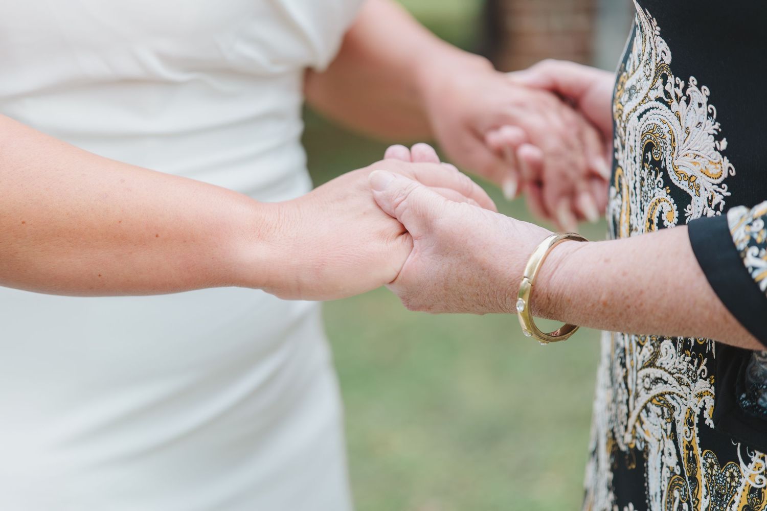 Close-up shot of two people holding hands during an outdoor wedding ceremony with white dress and ornate details visible.