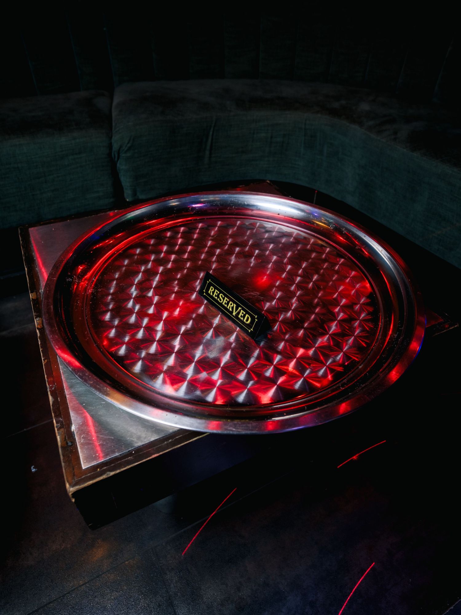 Red illuminated serving platter with geometric pattern and metallic trim in dark moody lighting.