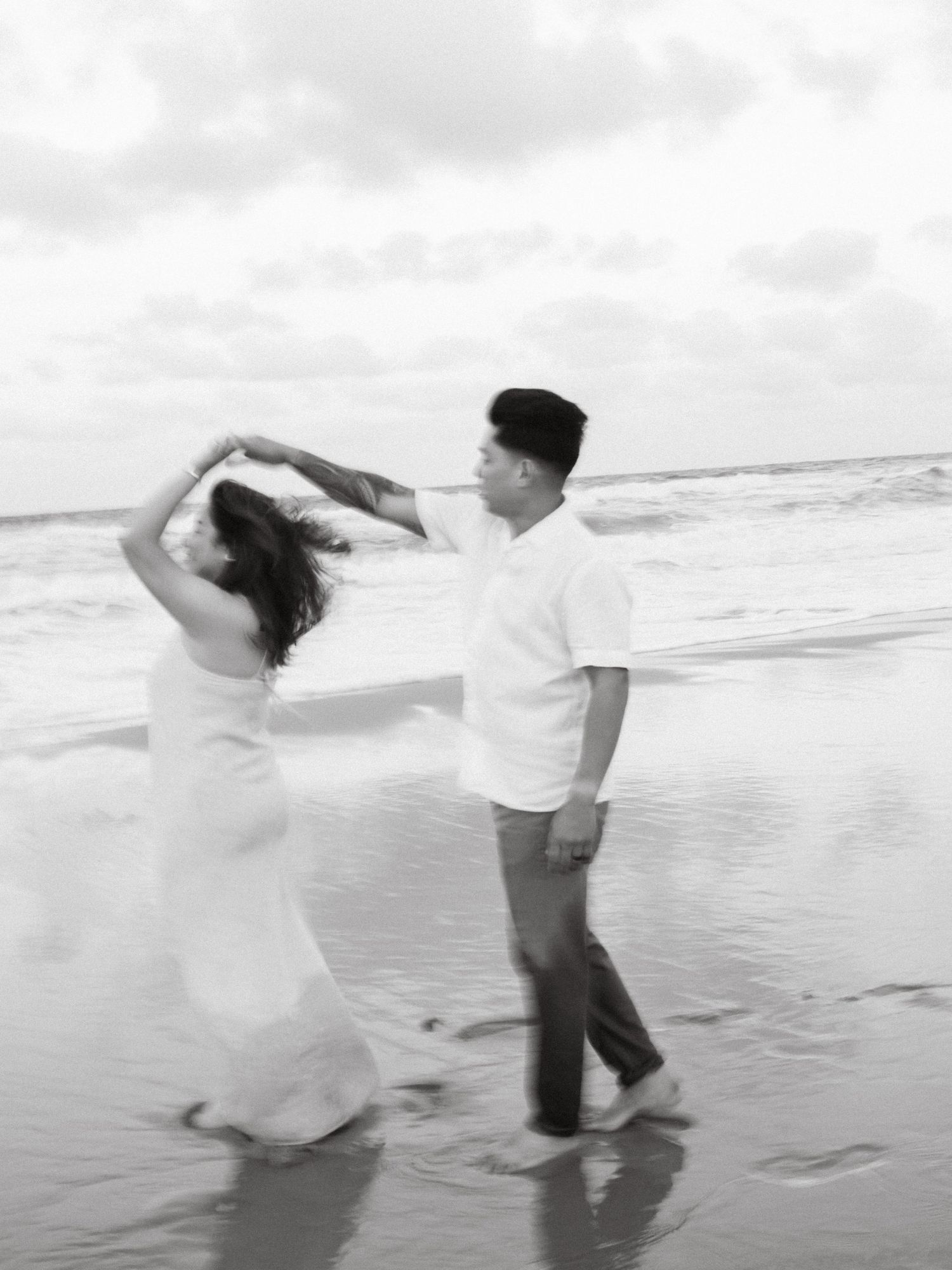 Couple dancing and twirling together on beach in black and white photography.