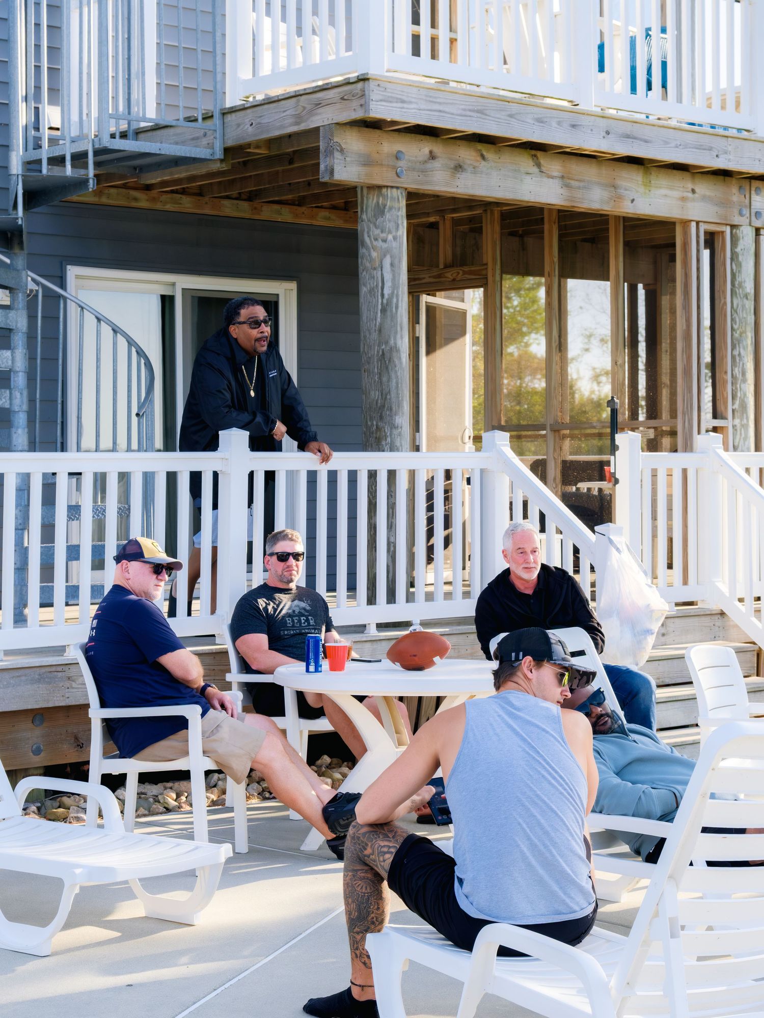 Group relaxing on white deck chairs on a porch with railing during a casual outdoor gathering.