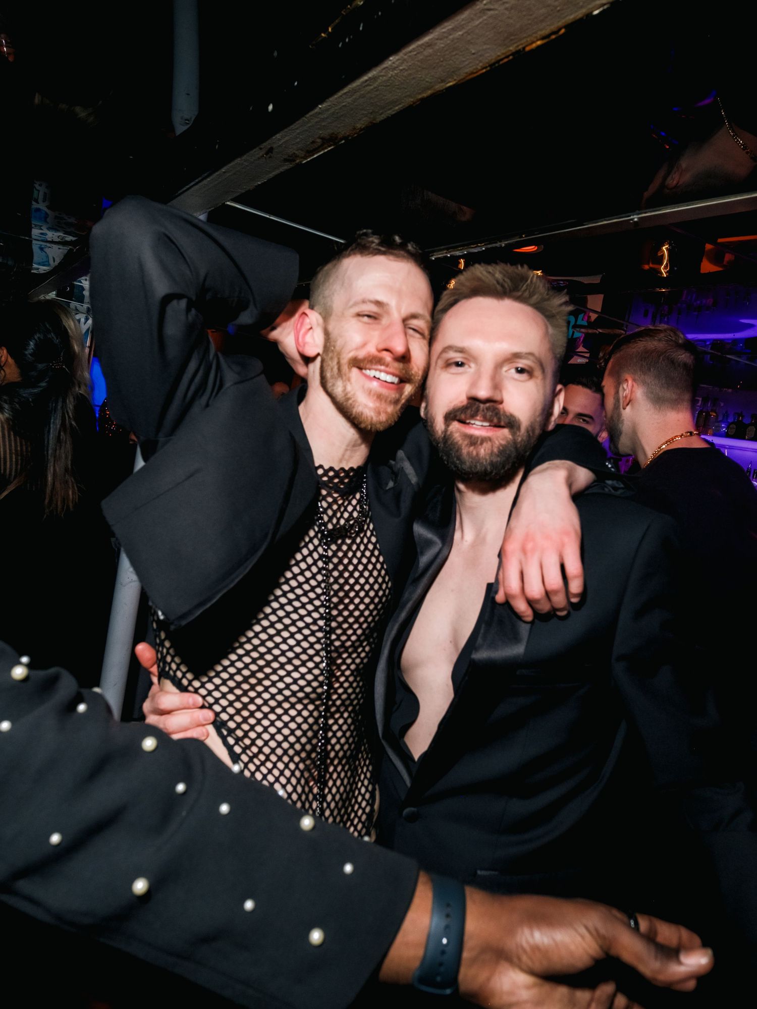Two friends enjoying a night out together at a club, one wearing a mesh shirt and one in black.
