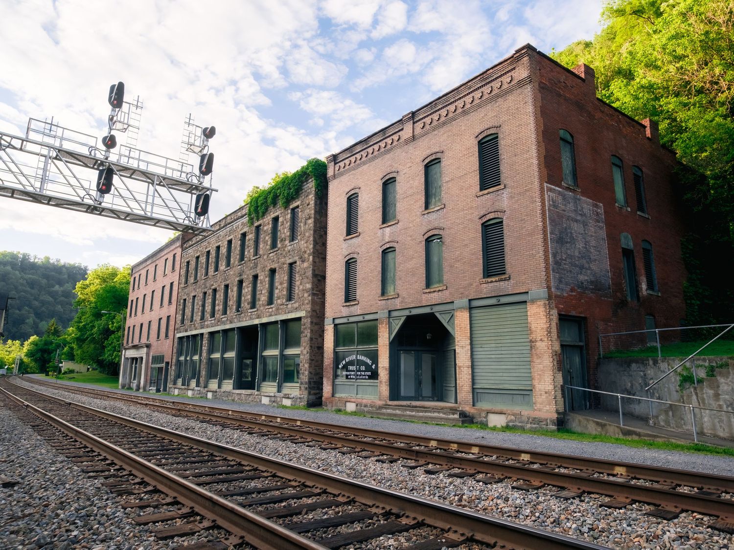 Historic brick buildings along railroad tracks in Thurmond, West Virginia with green mountains and signal tower in background.