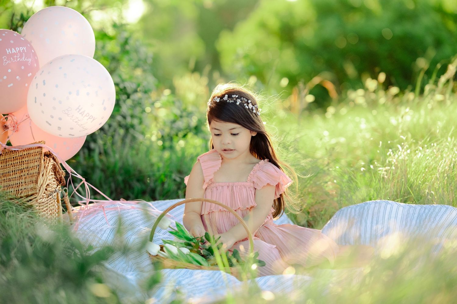 A spring photoshoot in a garden features soft pink accents, balloons and dreamy lighting among blooming foliage.