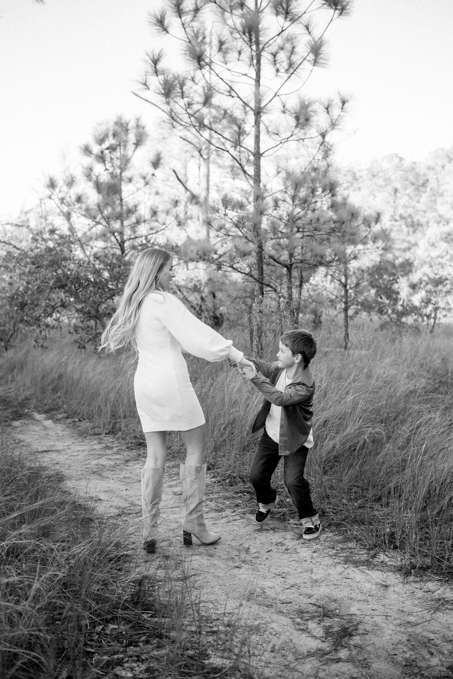 Black and white series of photos showing parent and child playing together on a nature trail among tall pine trees.