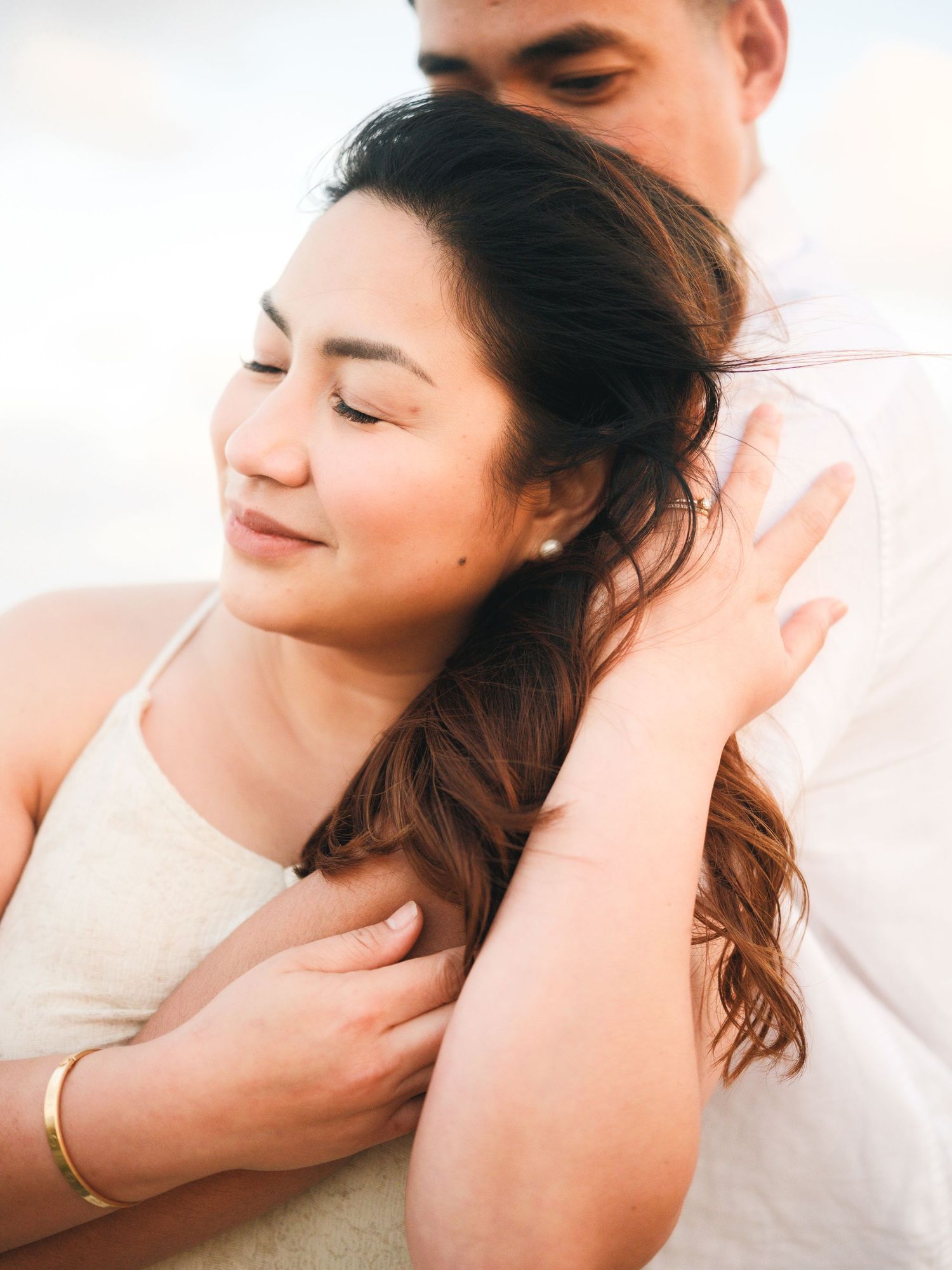 Soft intimate portrait of couple in natural light against white background.