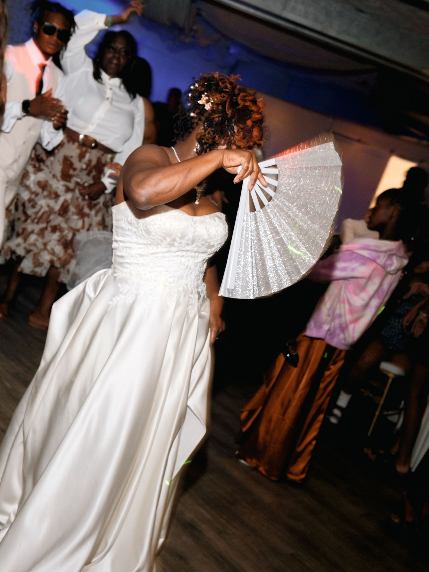 A person in a white wedding dress dances with a decorative fan at a reception celebration.