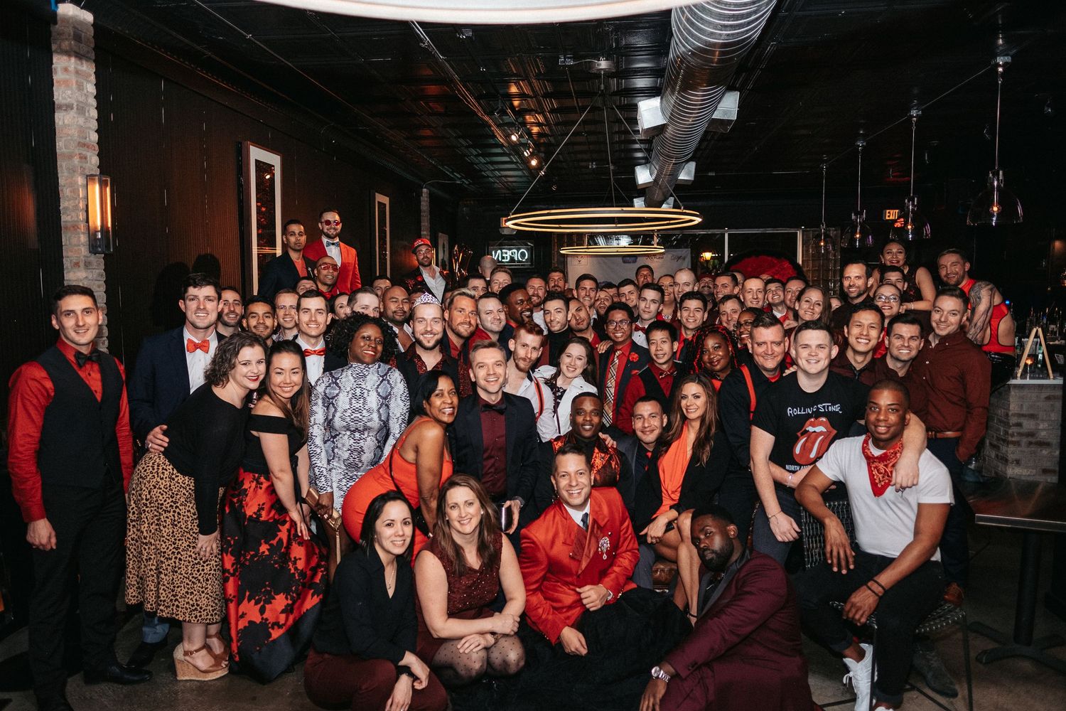 People gather in a dark indoor space wearing red and black clothing during what appears to be a social event.