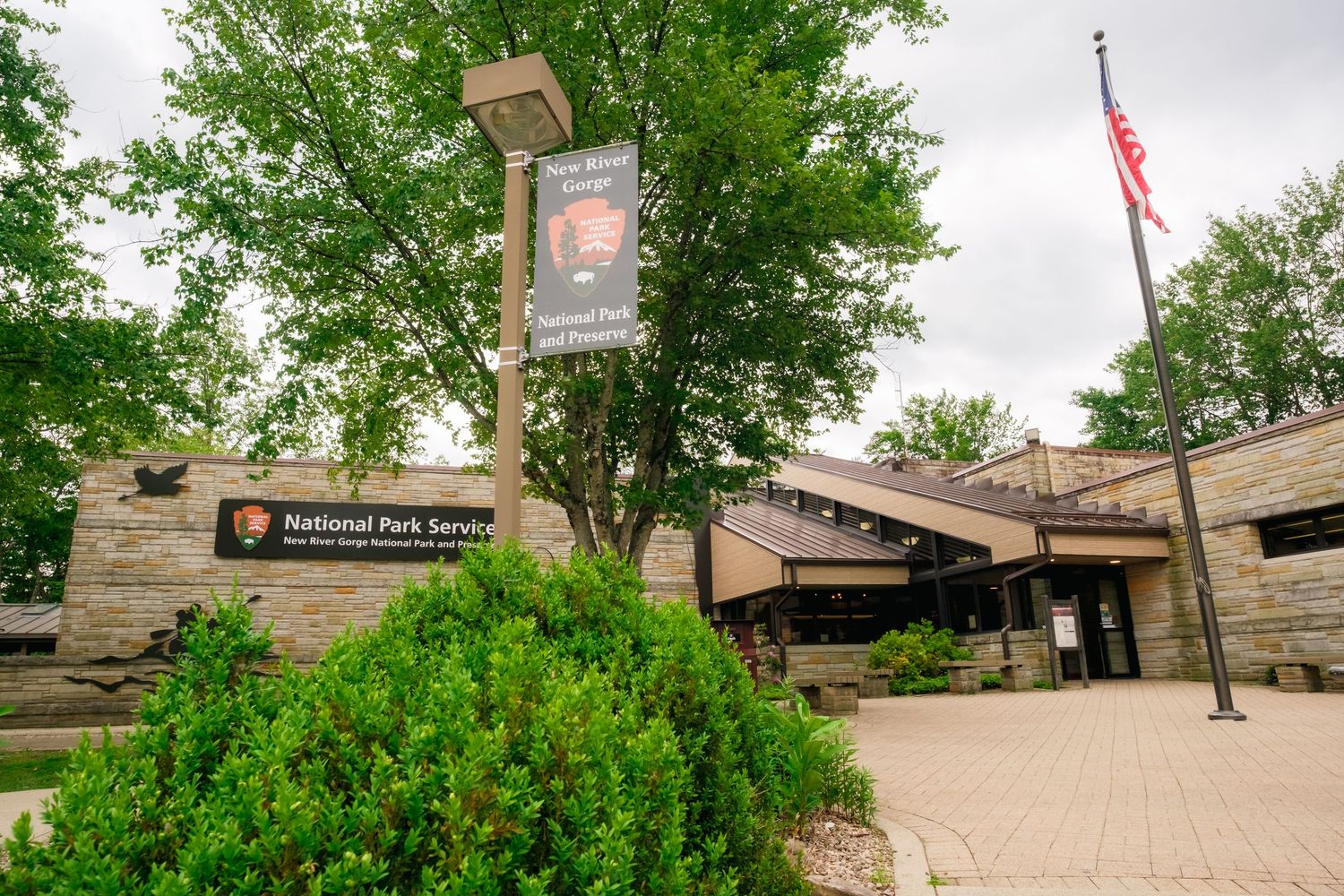 Entrance to the National Park Service visitor center with an American flag and green landscaping on a cloudy day.