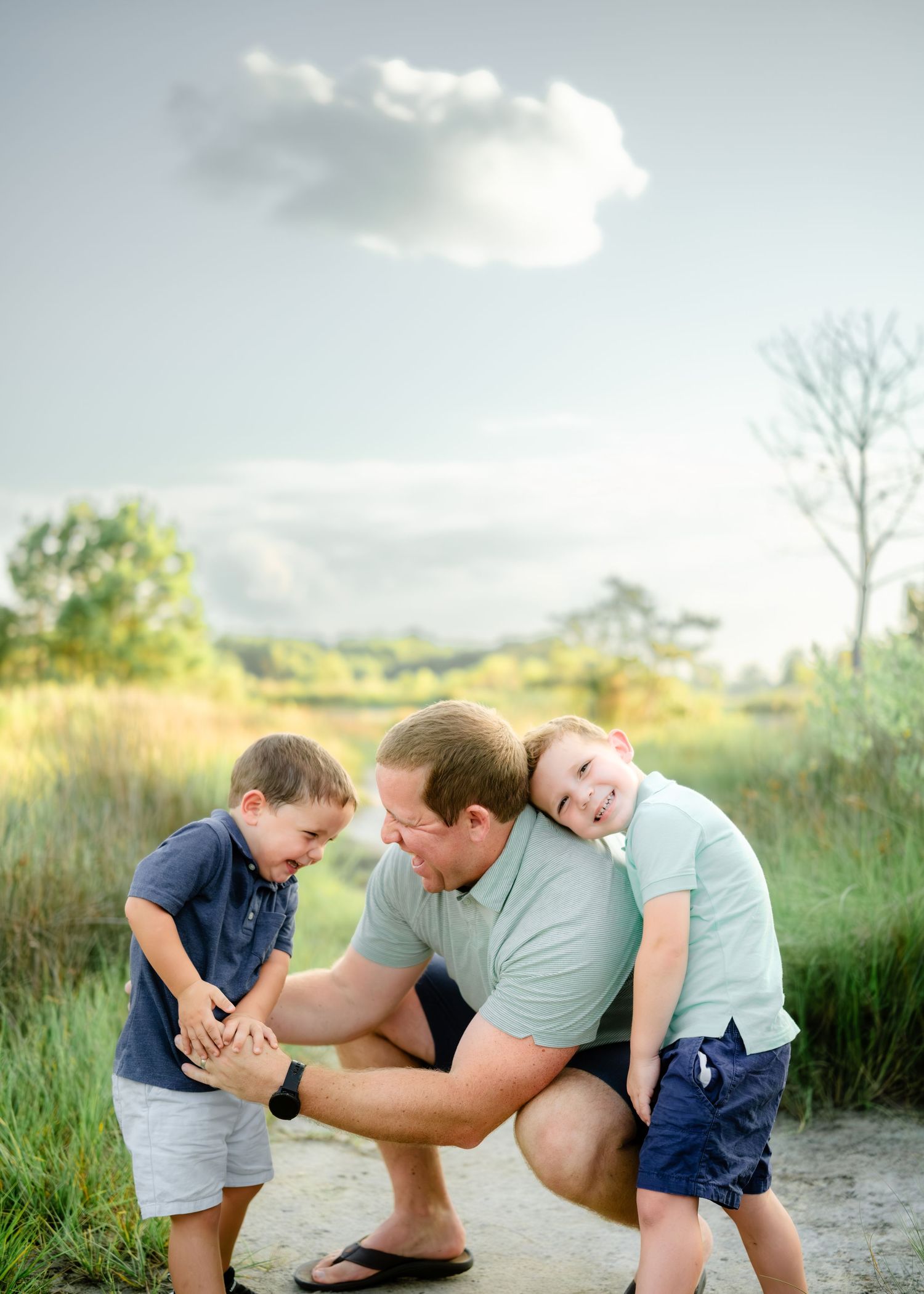 Two people playfully wrestling and roughhousing together outdoors in a grassy field during summer afternoon light.