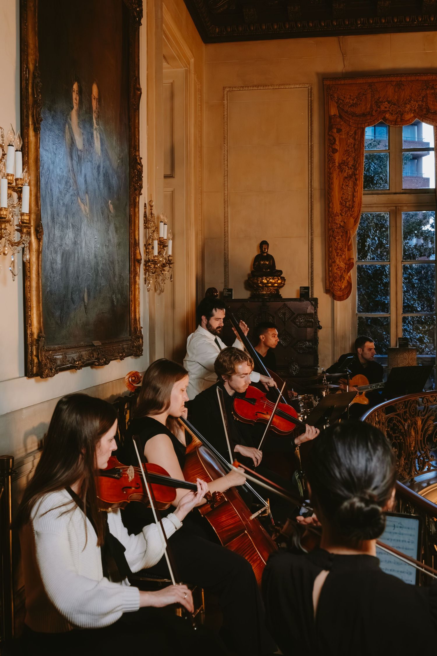 String quartet musicians perform in an elegant room with ornate walls, vintage decor and large windows.