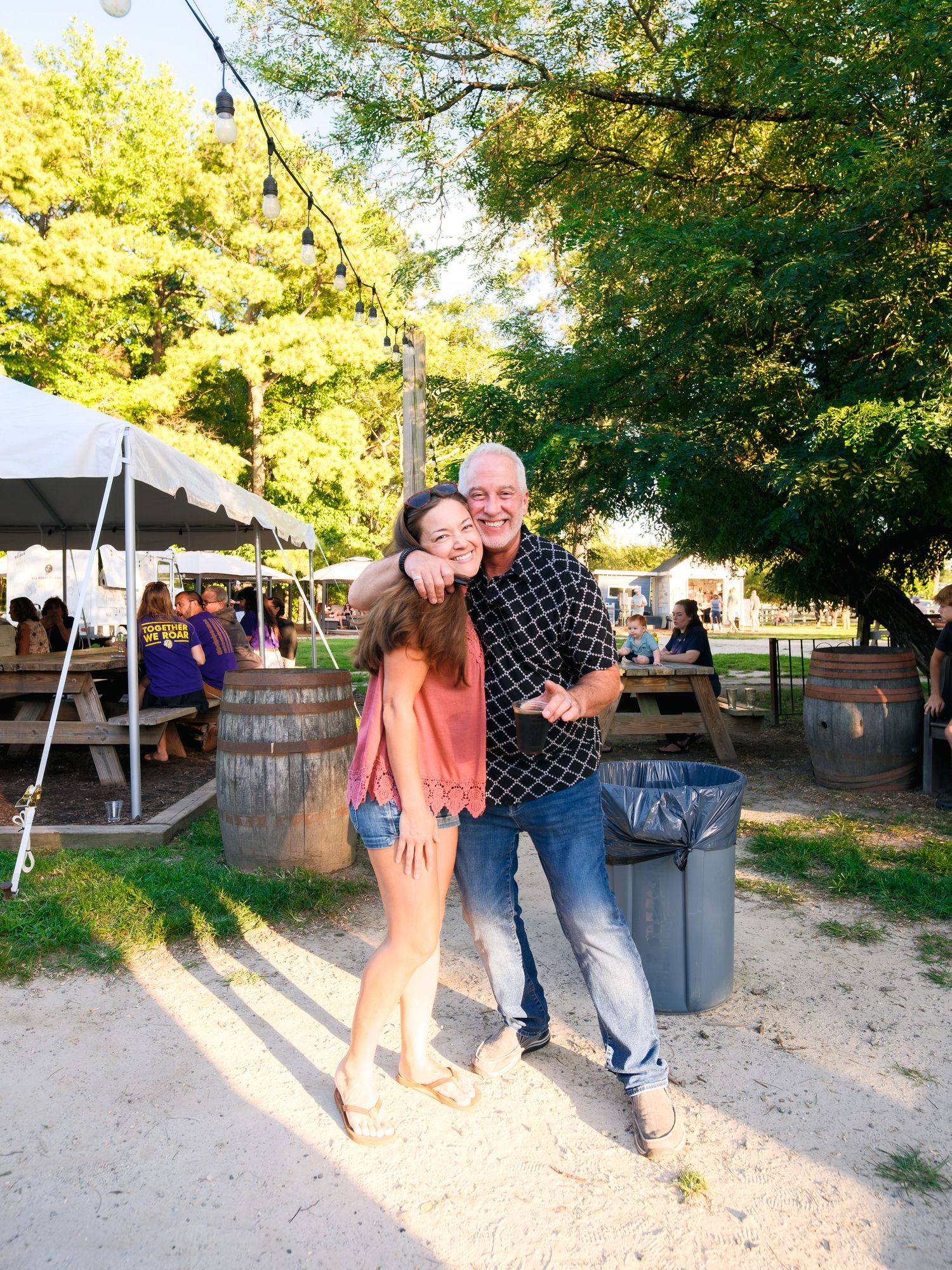A casual outdoor party scene with people mingling near trees at sunset.