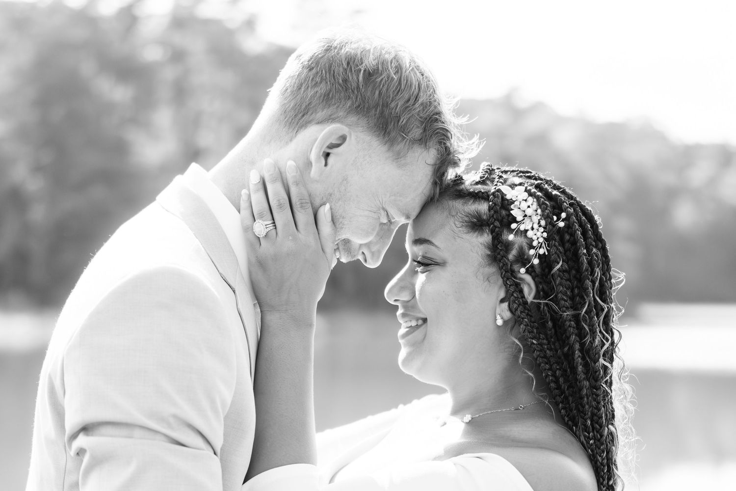 Black and white romantic wedding portrait of couple sharing an intimate moment by a lake.