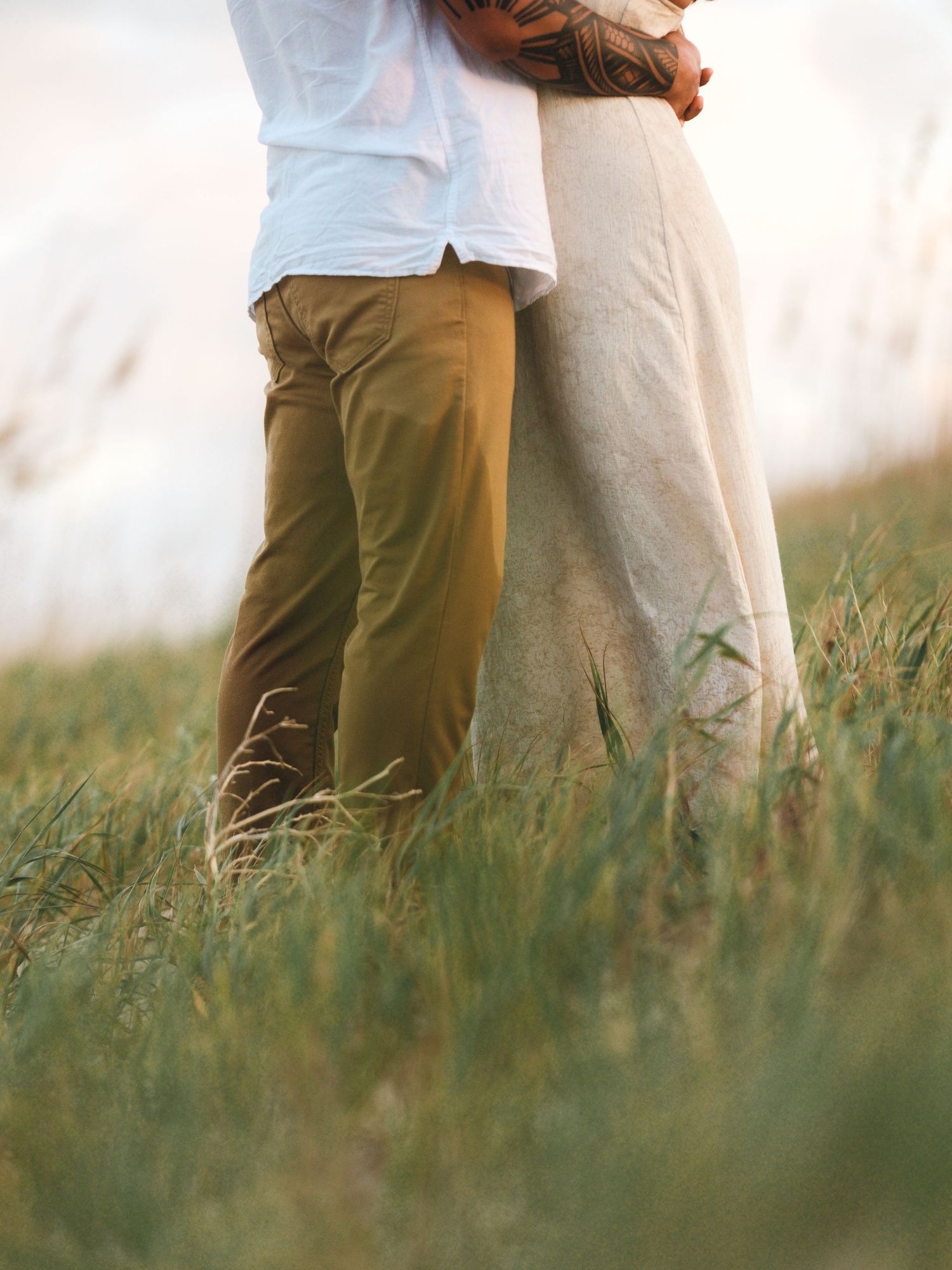 Lower body view of couple standing together in tall grass.