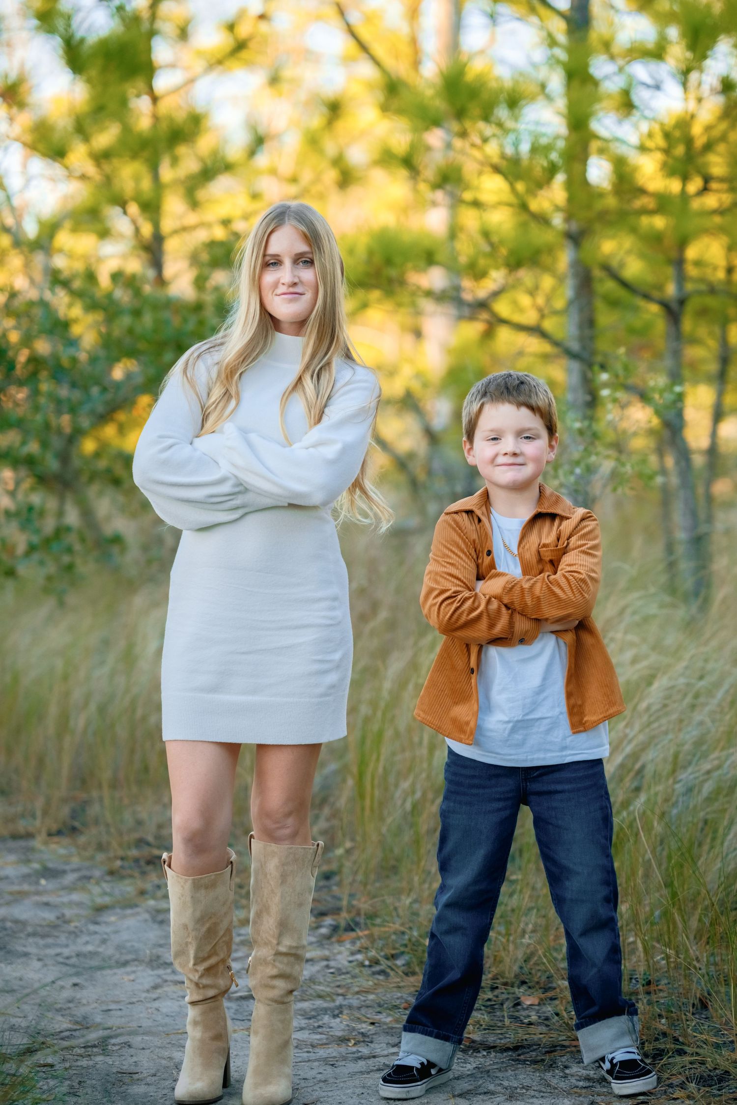 A casual outdoor photoshoot in autumn featuring a parent and child standing together among tall grass and trees.