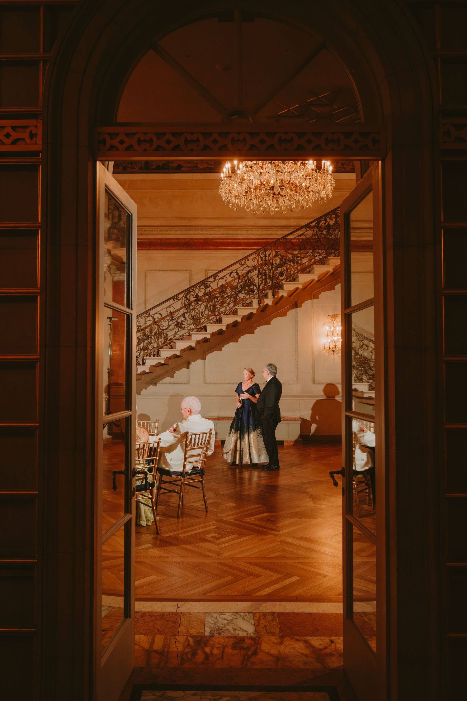 Elegant wedding photos captured through doorways show couples dancing in a grand ballroom with herringbone wood floors.
