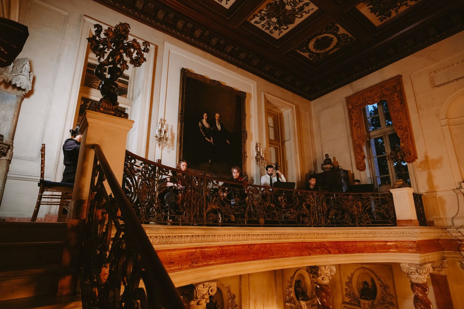 A grand ballroom with ornate chandeliers, gold trim details, and a painted ceiling in an elegant palace setting.