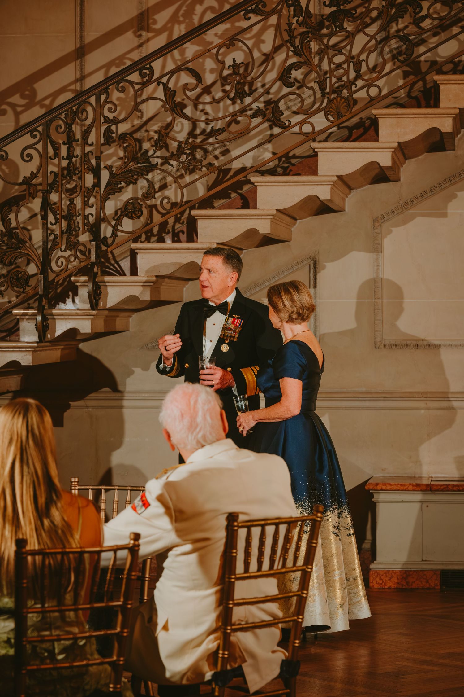 A romantic couple dances together on a wooden floor beneath ornate wrought iron railings at an elegant venue.
