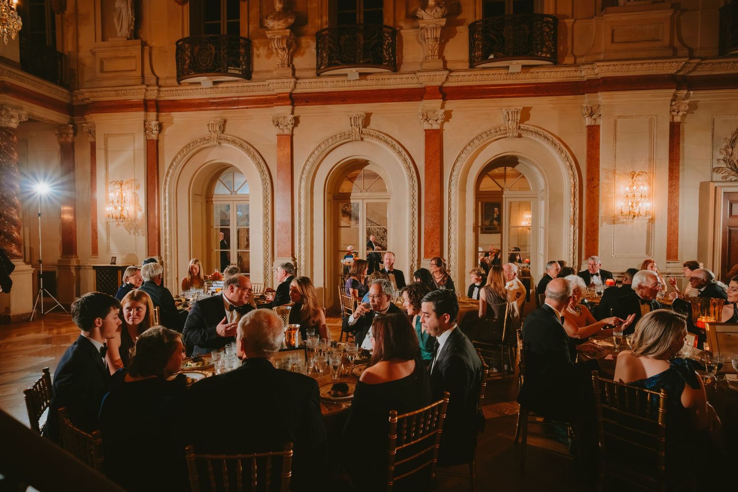 Wedding guests enjoy an elegant reception dinner in a grand ballroom with warm lighting and ornate decor.