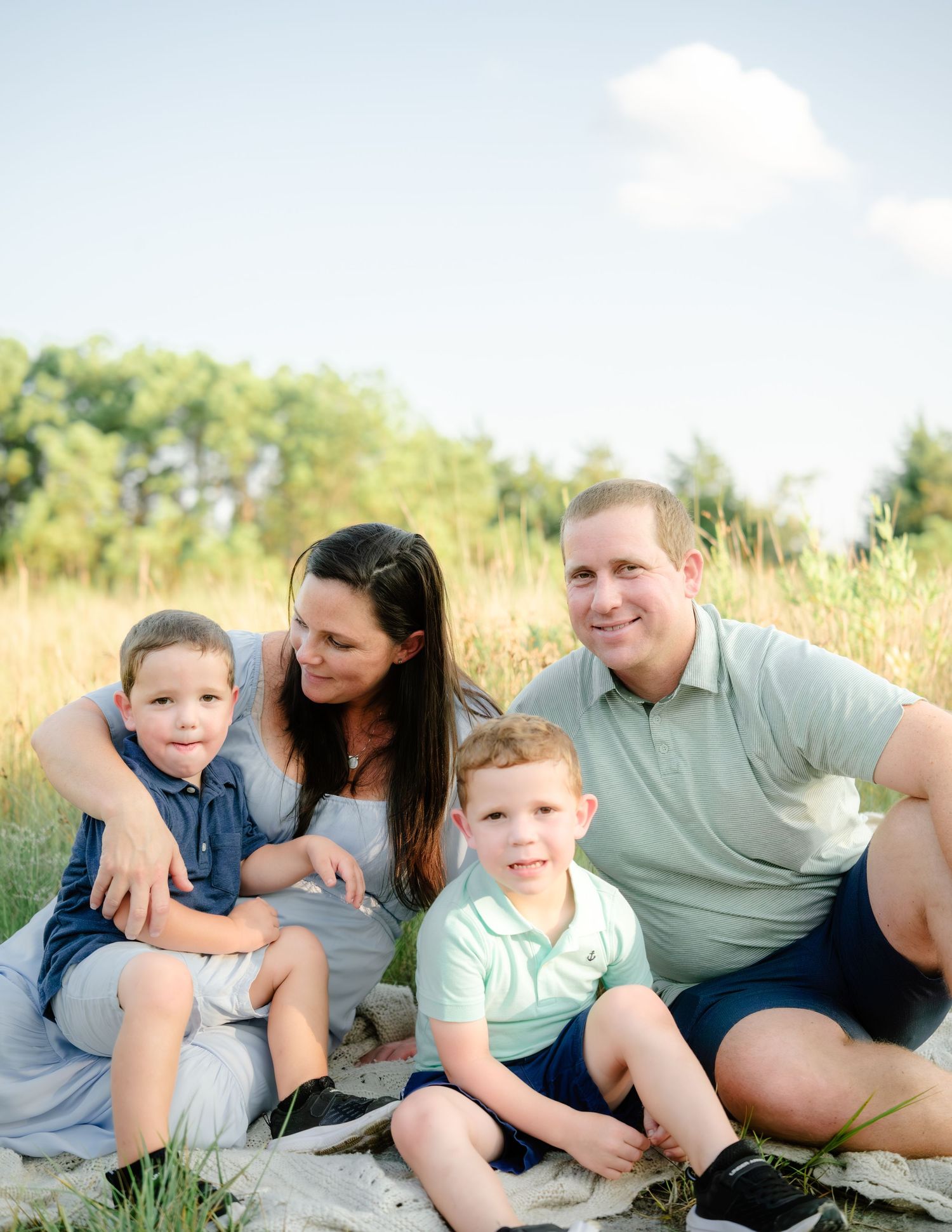 Family sitting together and sharing tender moments in a field at golden hour.