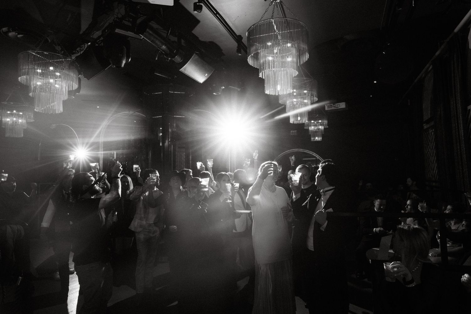 A black and white nightclub scene shows a crowded dance floor with bright spotlights illuminating the space.