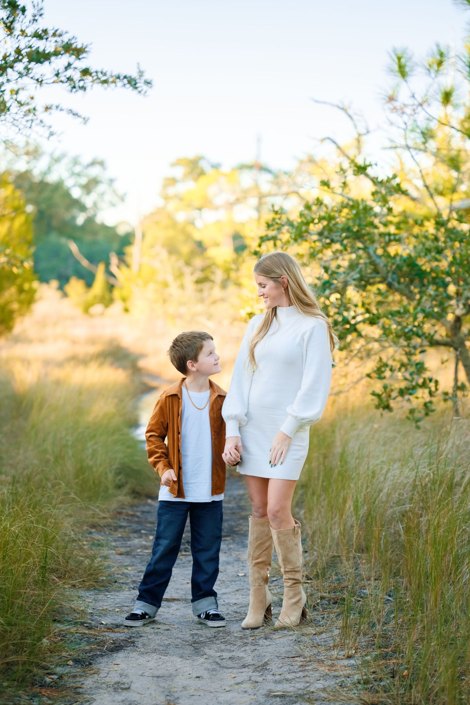 Family walking together on a sandy path through tall grass during sunset in a natural outdoor setting.