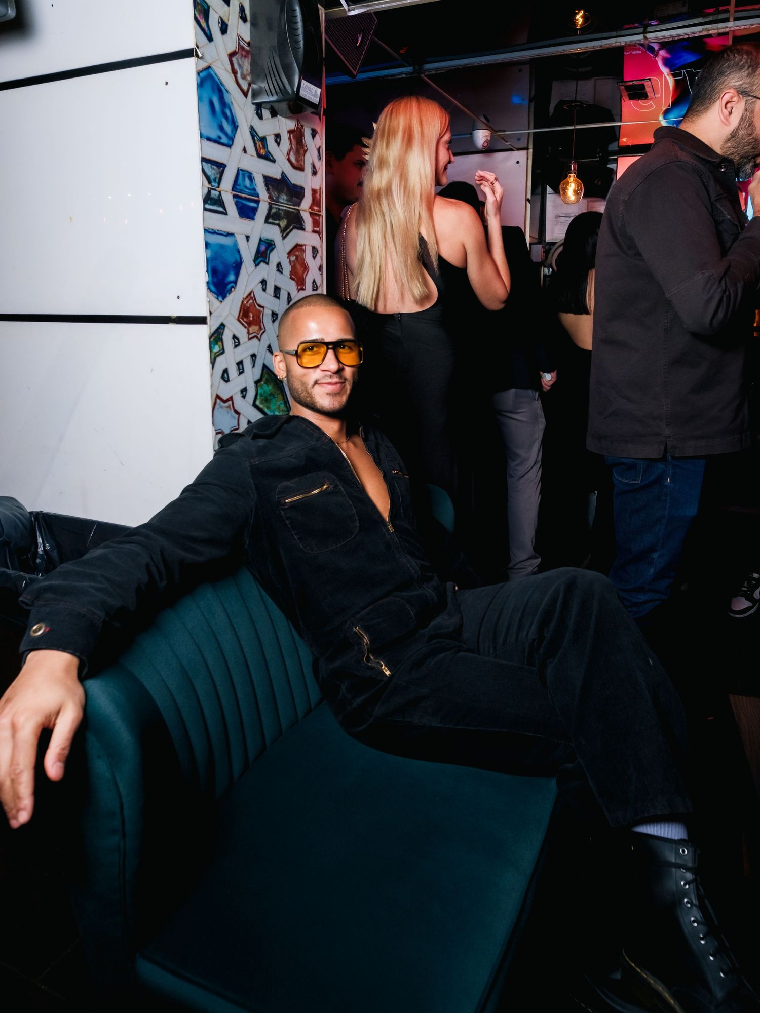People in black attire socializing at a nightclub with lighting and decorative elements in the background.