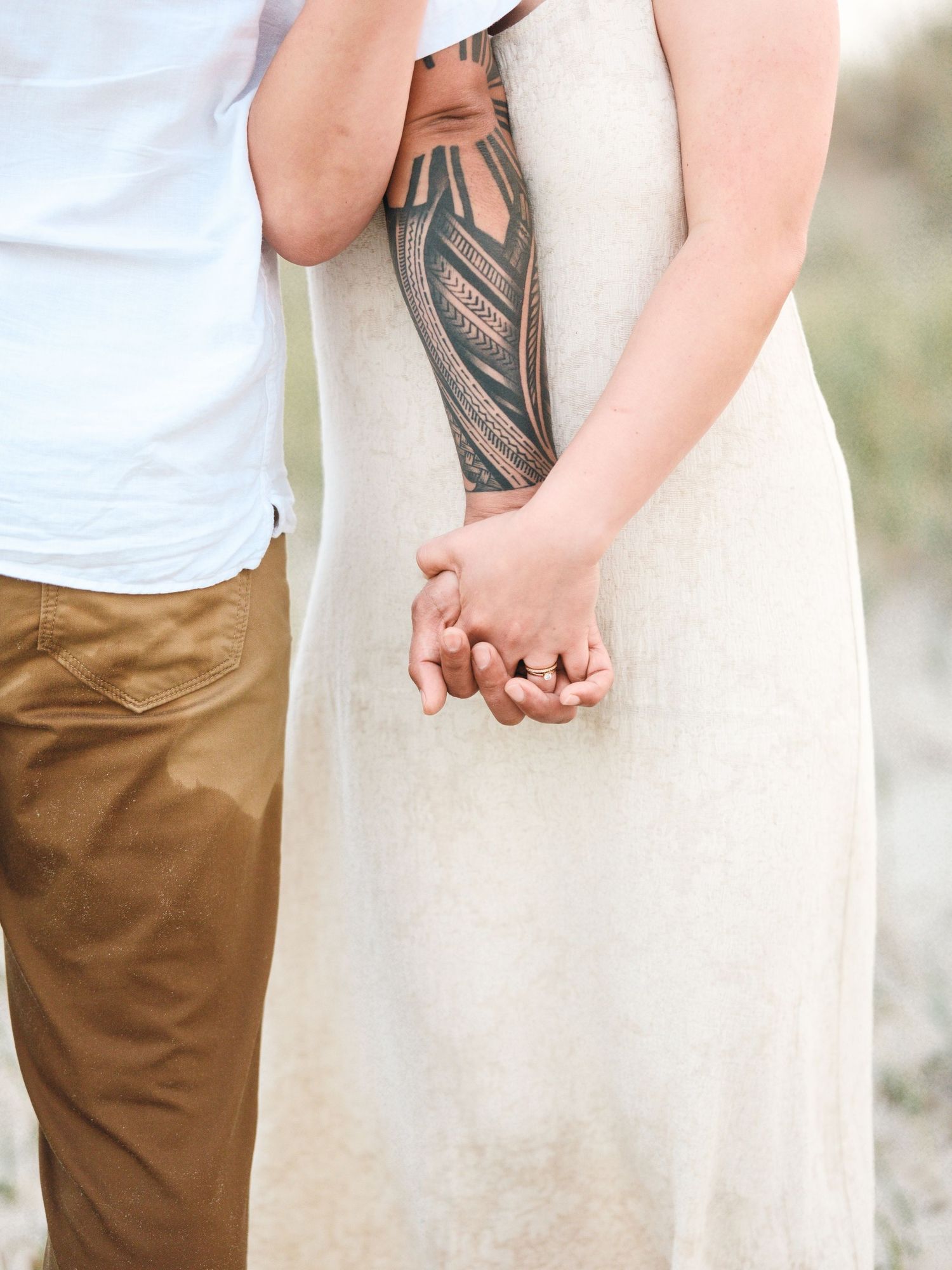 Detail shot of hands and tattoo against white dress and khaki pants on a beach.