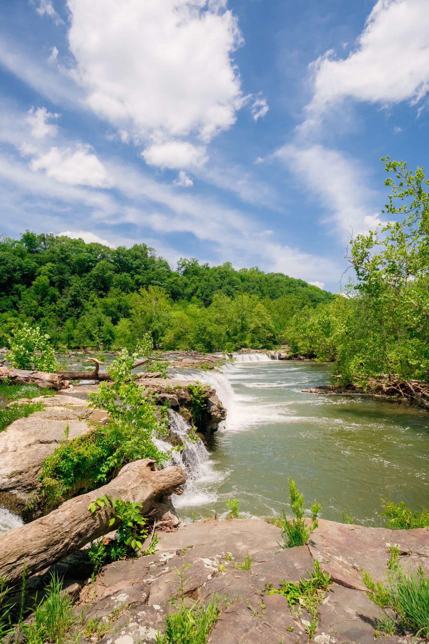 A scenic river with natural rock outcrops and greenery winds around through a sunny summer landscape under blue skies.