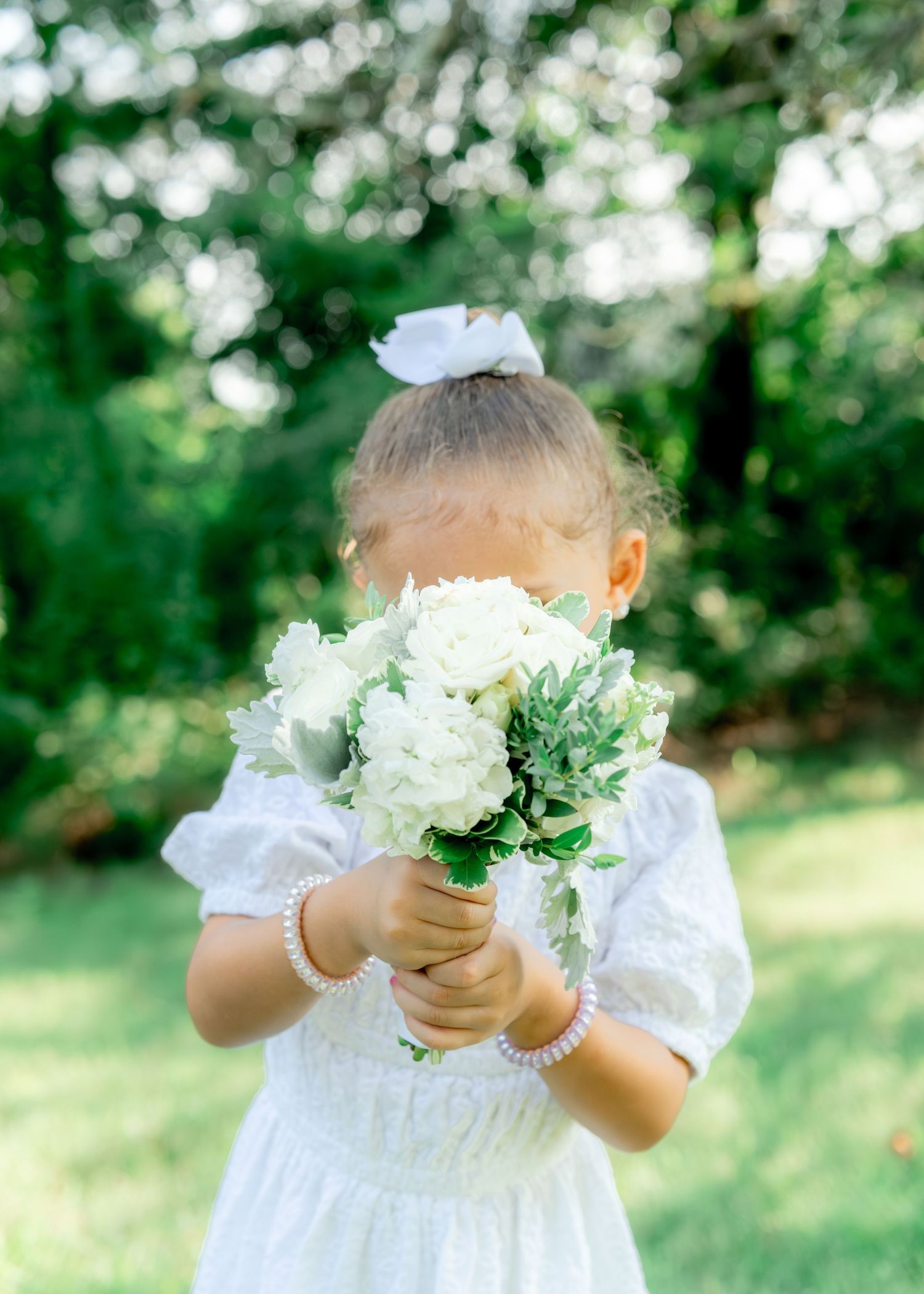 Small hands holding delicate white flowers against a soft green garden backdrop, creating a dreamy outdoor scene.